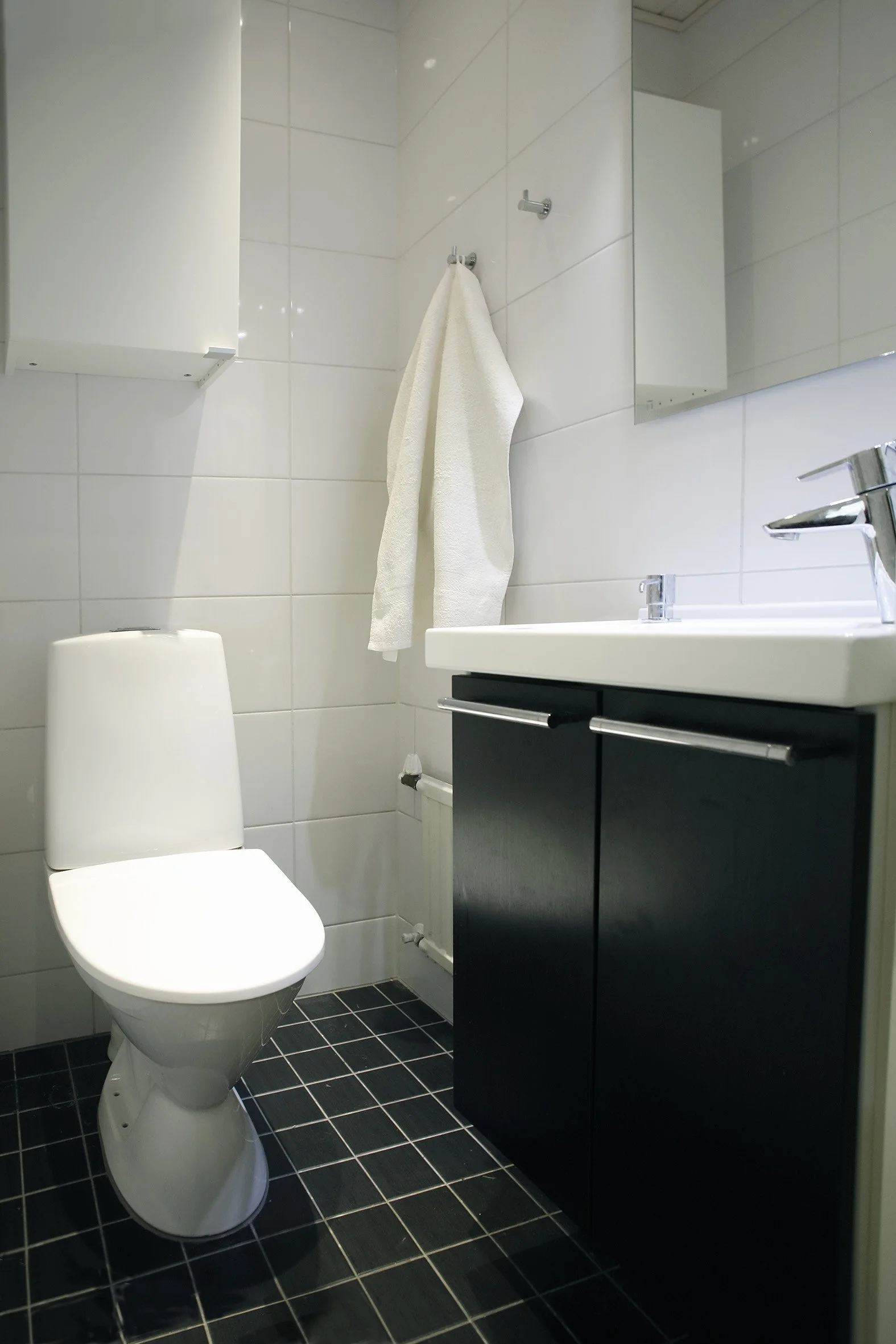 Kylpyhuone, jossa wc-istuin, valkoinen pesuallas ja suuri peili seinällä.