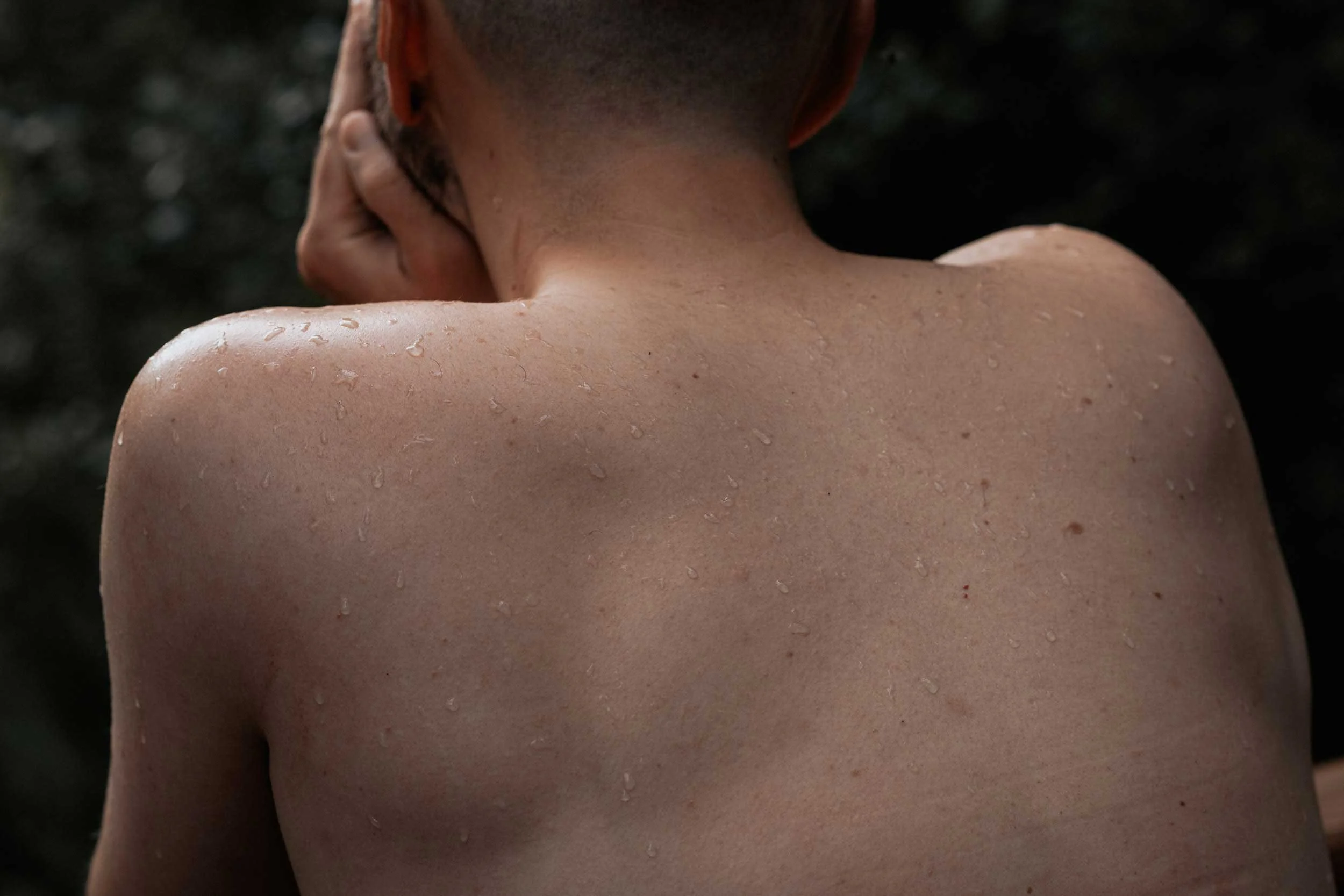 Topless man looking out onto pond. Head in hands. Sweat on his shoulder