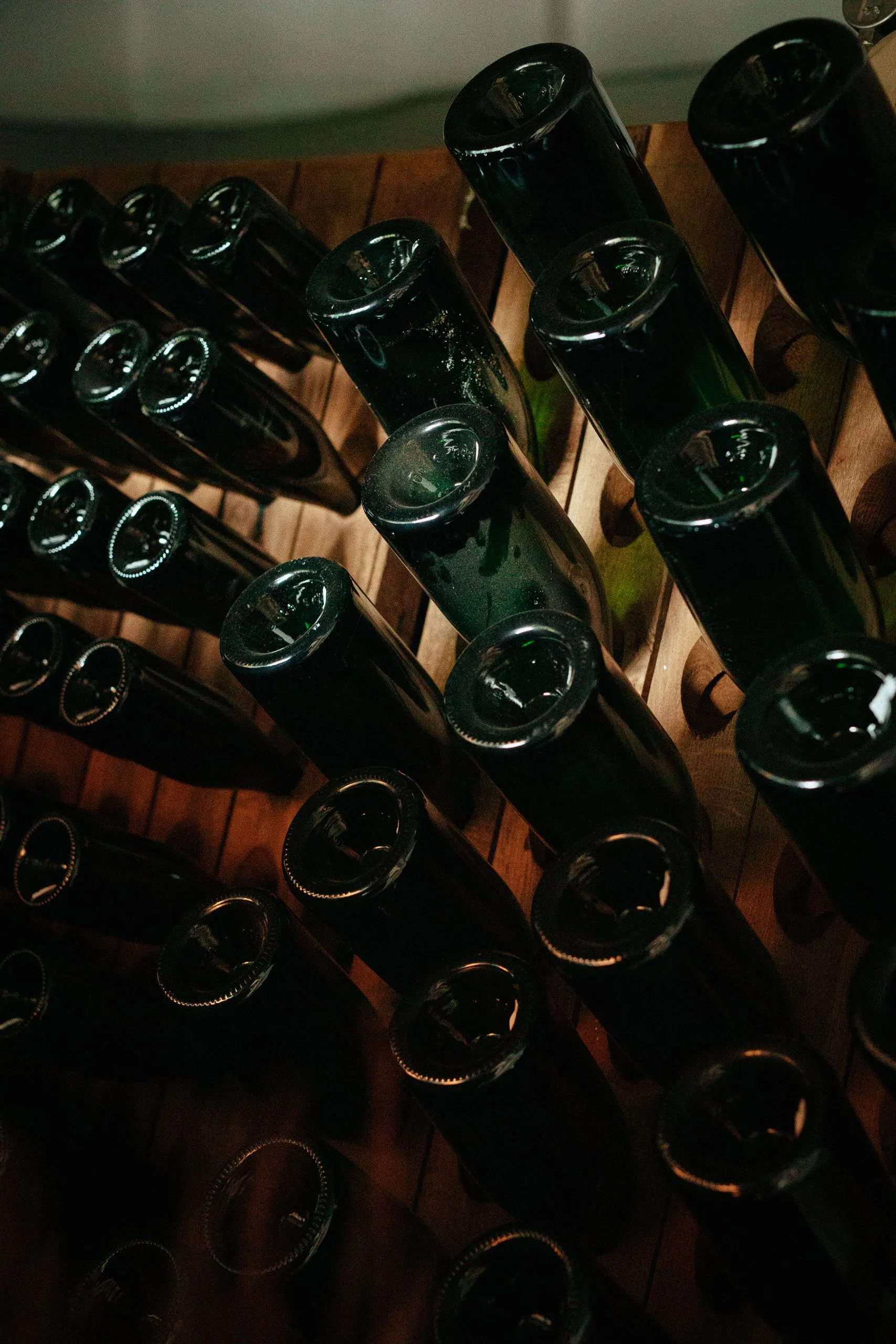 Rückansicht von mehreren grünen Weinflaschen in Holzgestellen gestapelt.