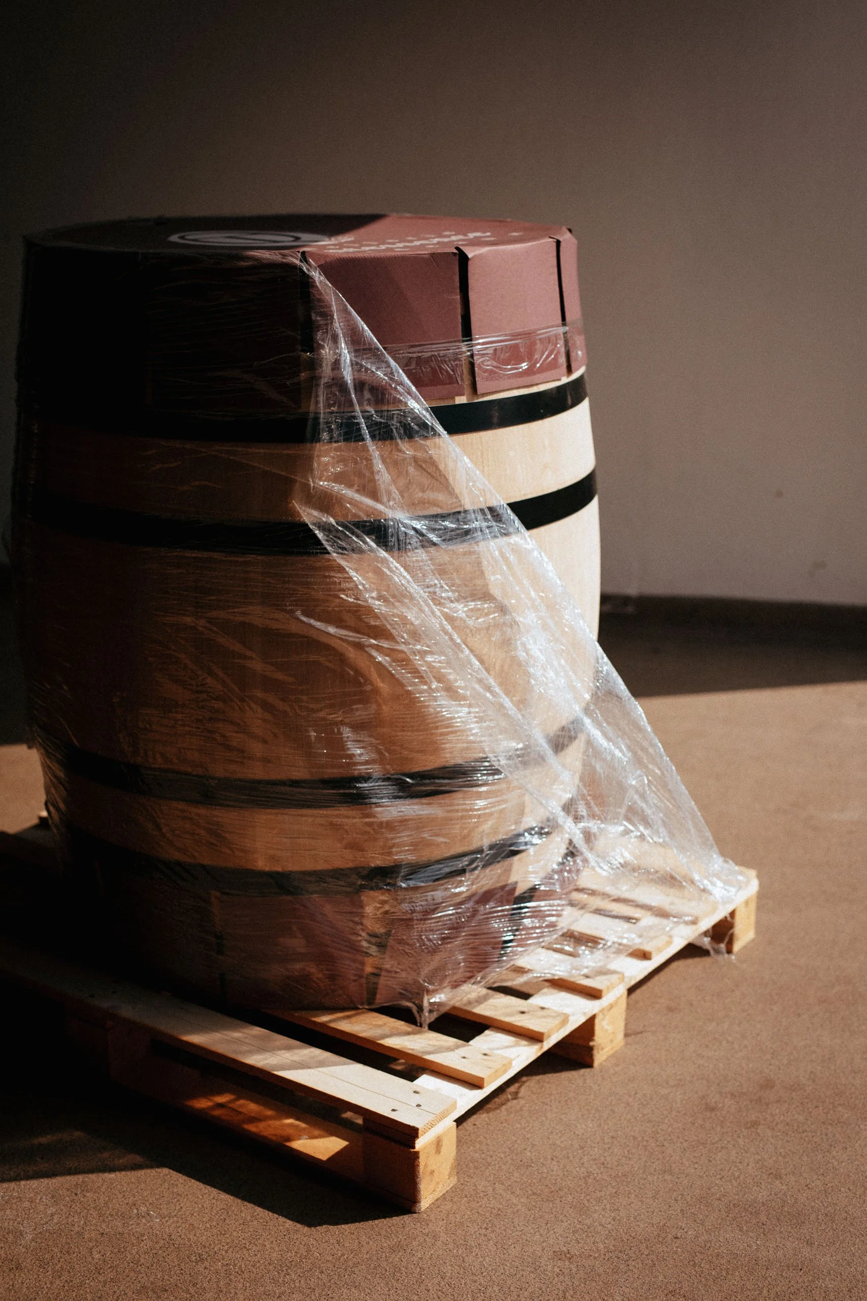 Holzfässer auf einer Palette, eingewickelt in transparente Folie, vermutlich für Lagerung oder Transport