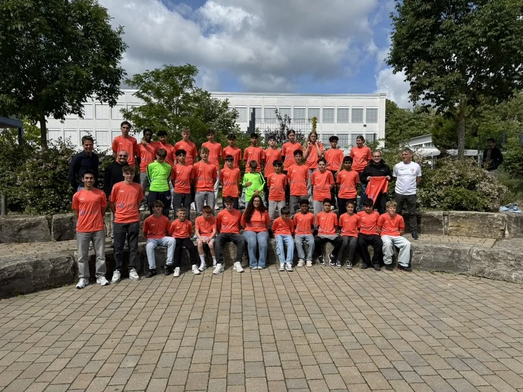 Gruppe junger Leute, die auf einer Treppe im Freien für ein Foto posieren, alle tragen ähnliche rote T-Shirts.