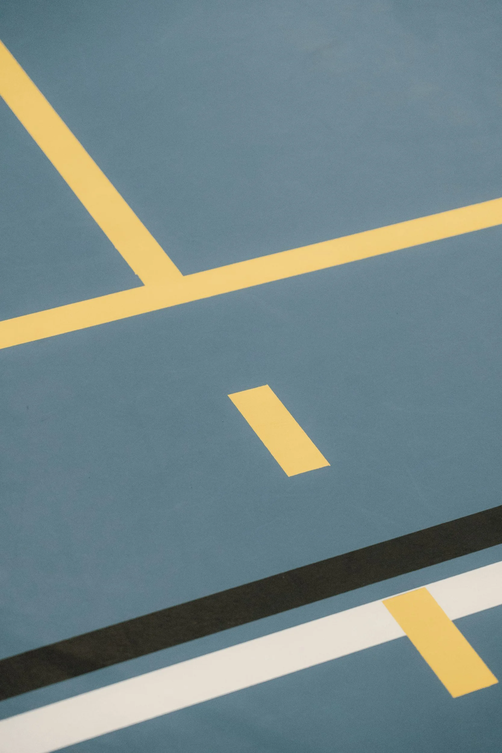 Close-up photograph of a blue parking lot surface with yellow, white, and black painted lines.