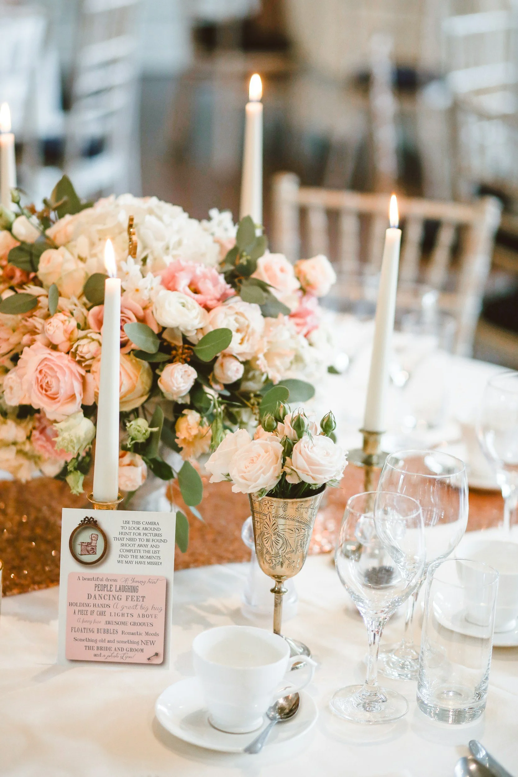 Elegant table centerpiece with pink and white flowers, tall candles, and glassware at a wedding reception.