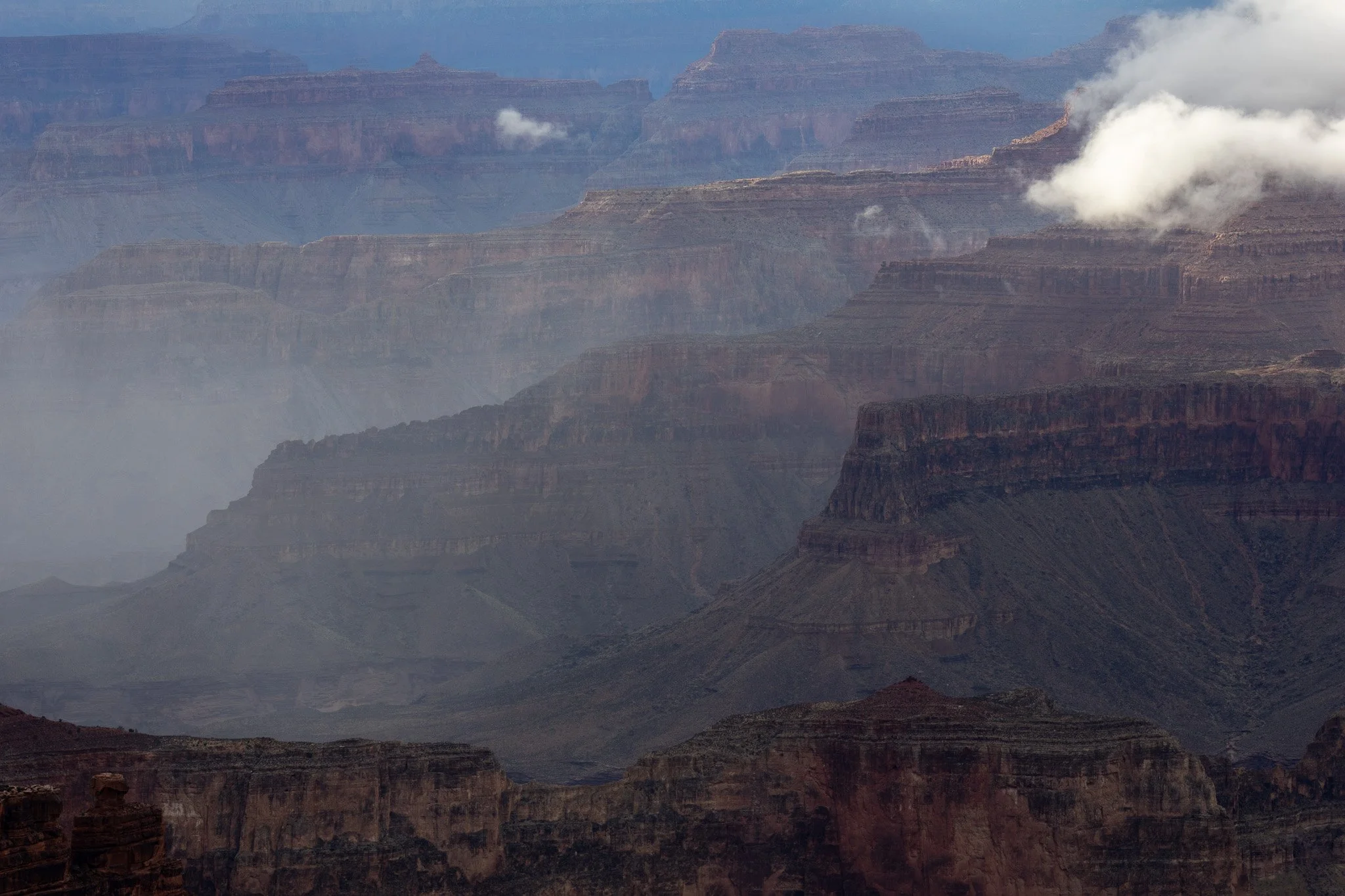 View of the Grand Canyon with layered rock formations, some clouds, and mist.
