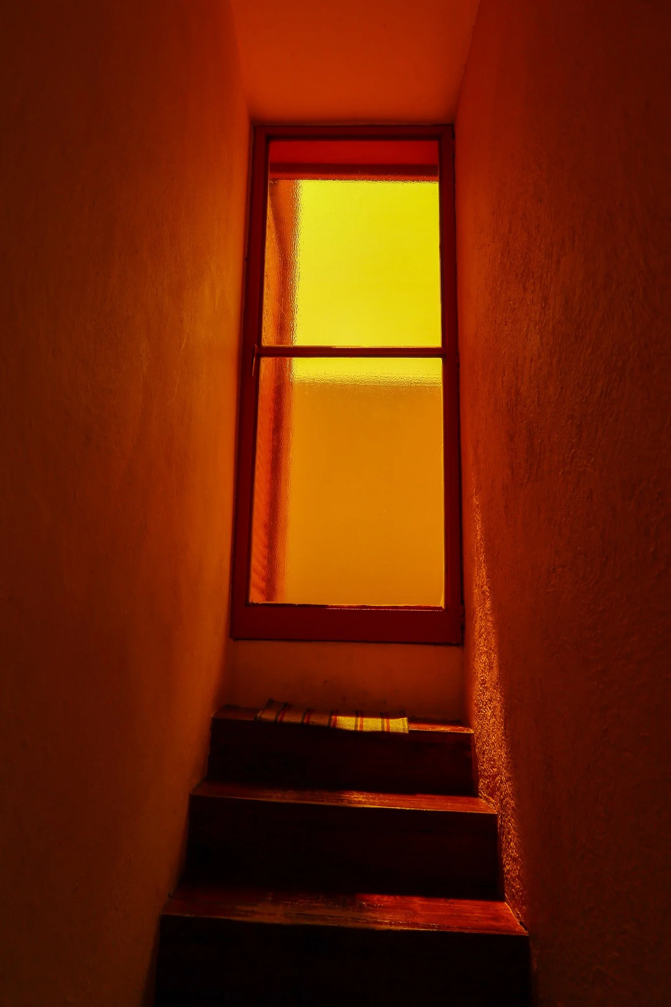 Backlit staircase with wooden steps and frosted glass window with yellow-orange tint, viewed from below.