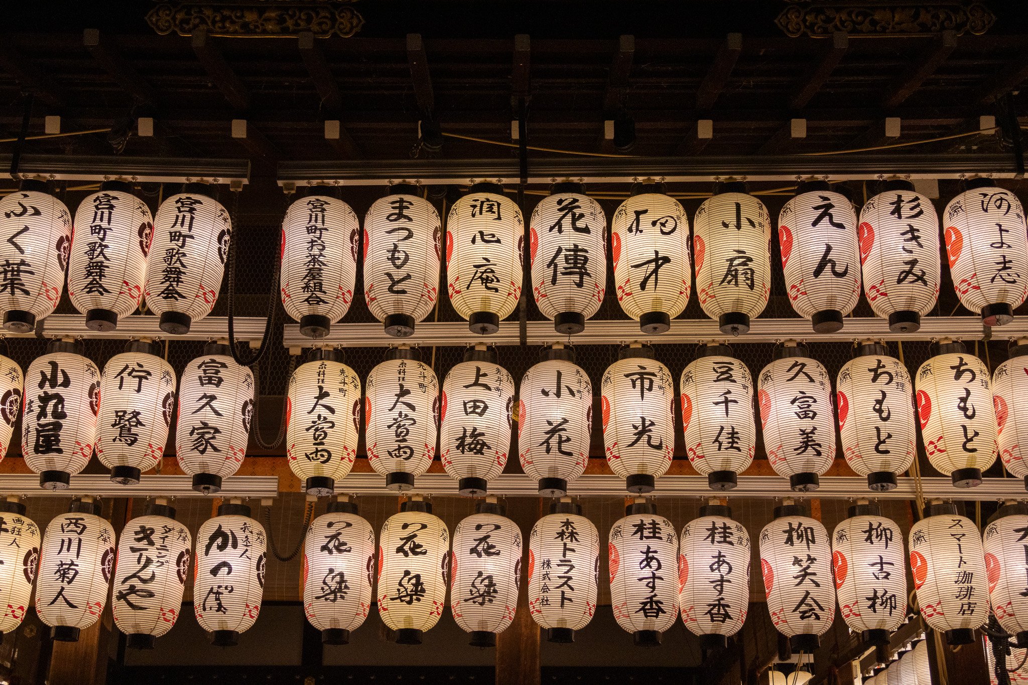 Japanese paper lanterns with black calligraphy hanging in rows at night.