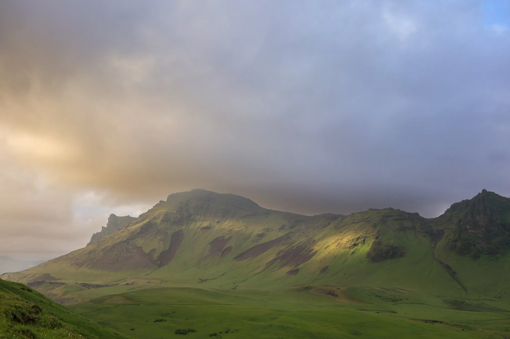 Green, mountainous landscape with rolling hills and a cloudy sky.