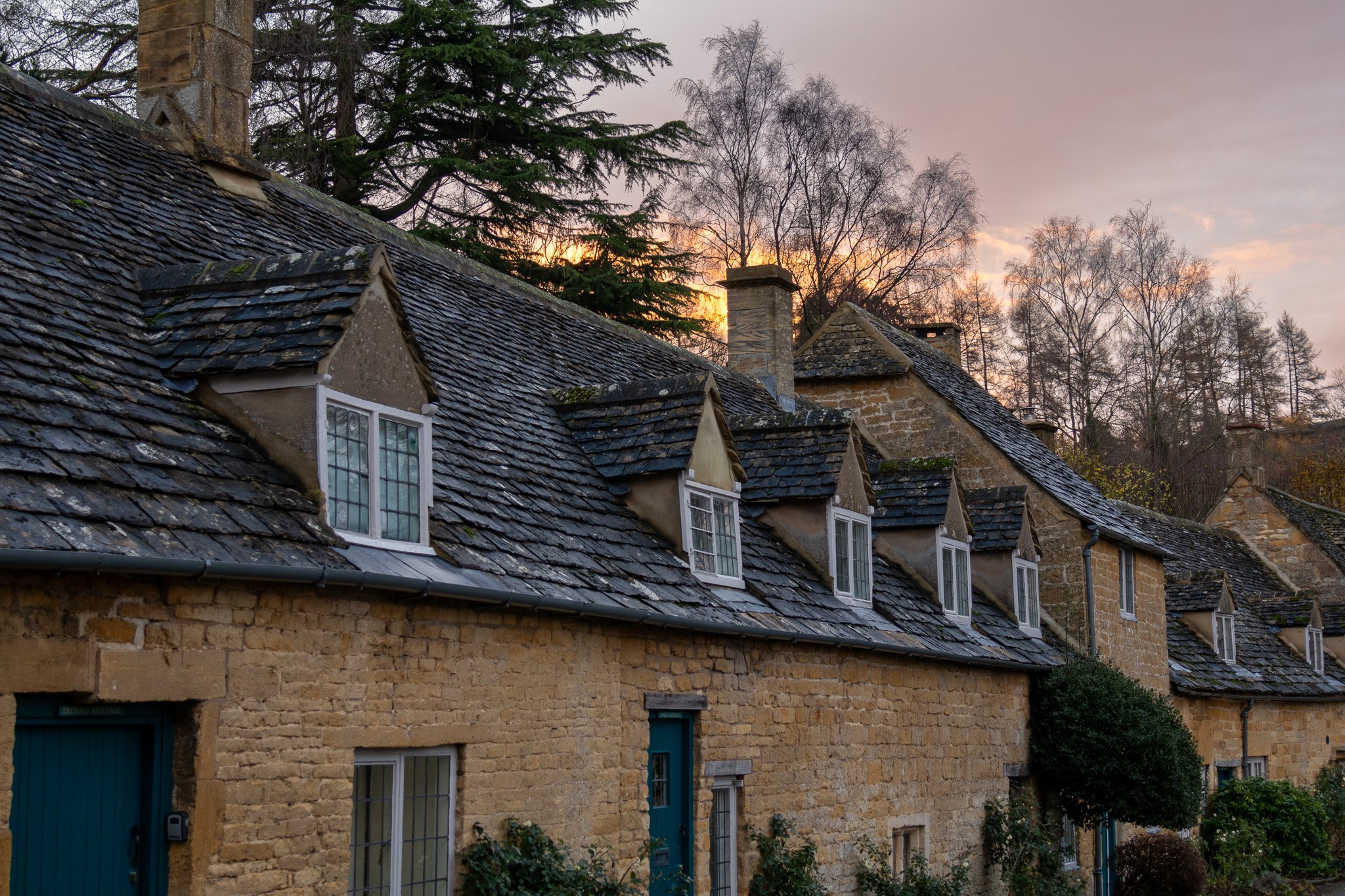 Row of historic stone cottages with gabled dormer windows and slate roofs at sunset.
