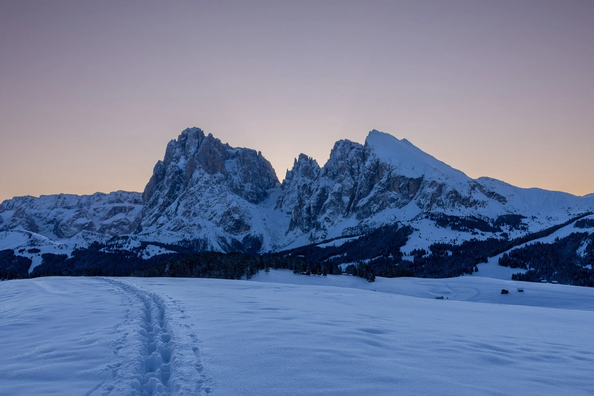 Snow-covered field with mountain range in the background during sunset or sunrise.
