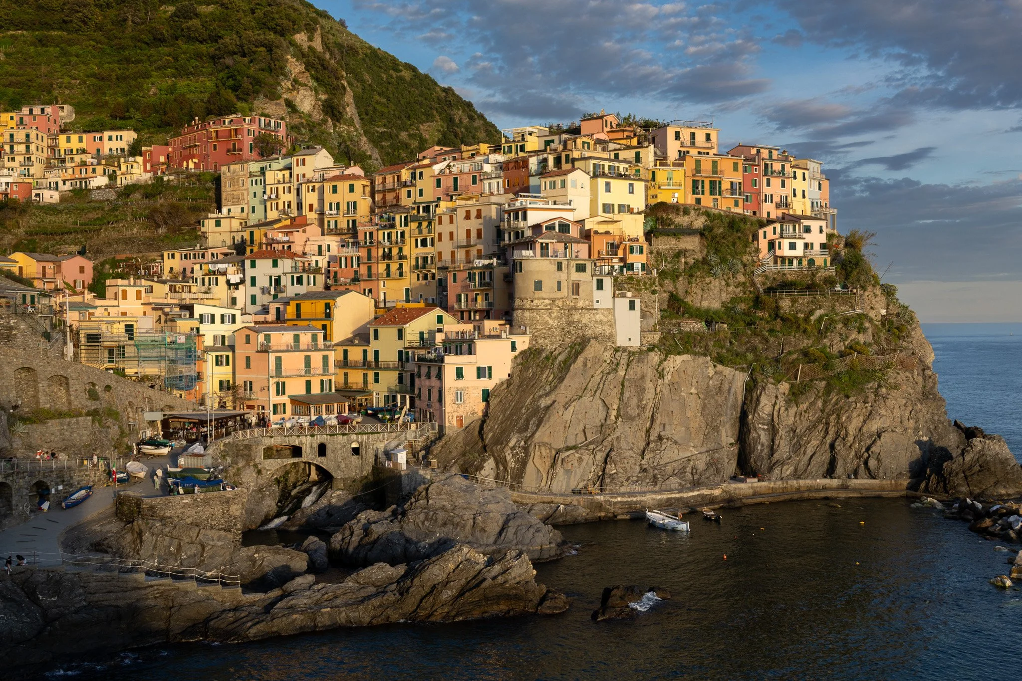 Colorful houses on a hillside by the water, with boats in a small harbor at sunset.