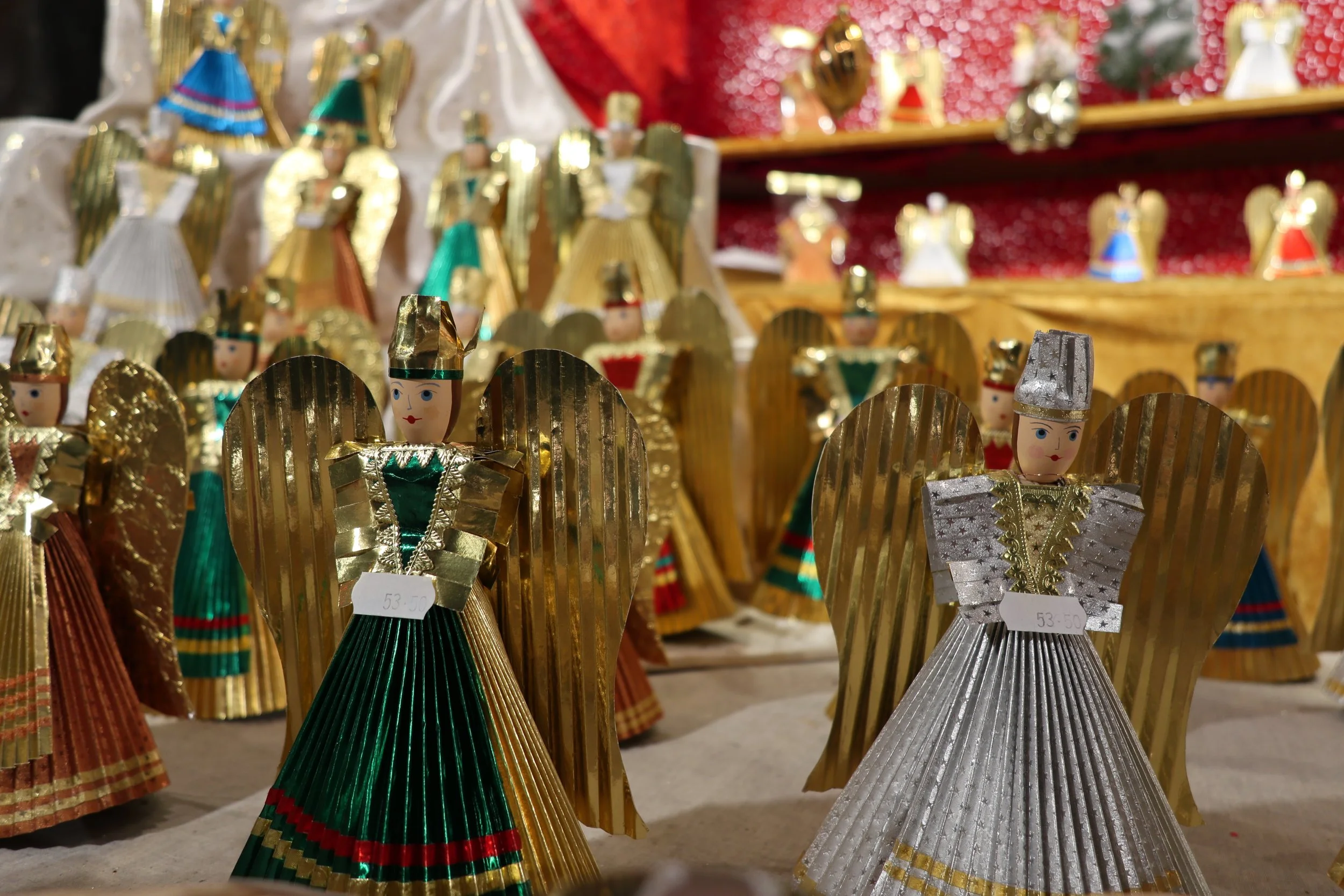Decorative Christmas angels made of shiny metallic materials in gold and silver, with painted faces, displayed in a store.