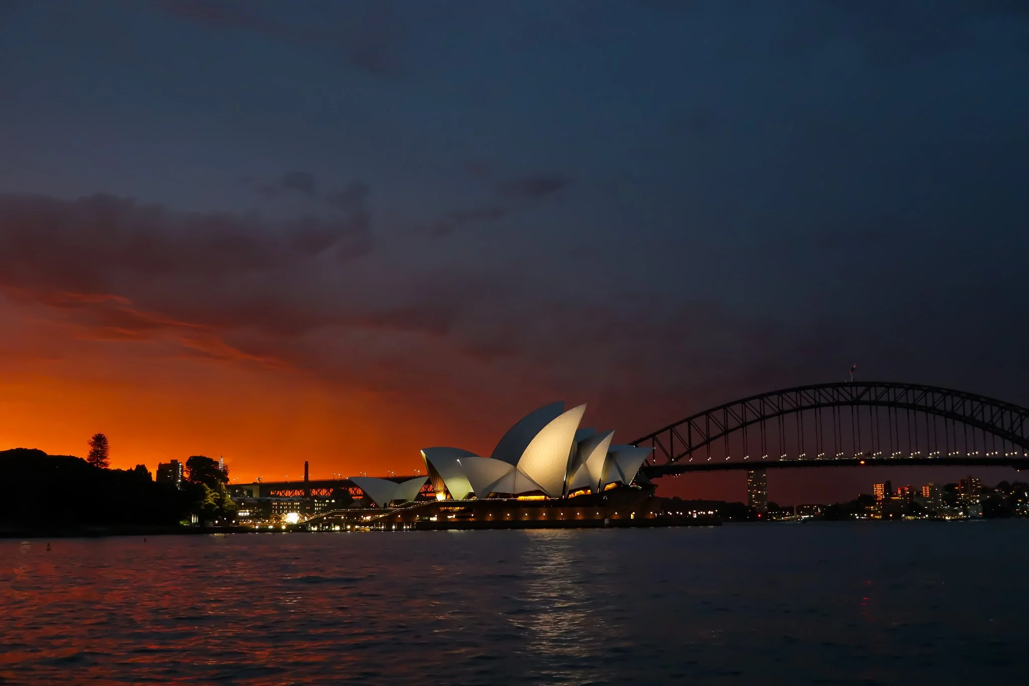 Sydney Opera House and Harbour Bridge at sunset, with a colorful sky and water in the foreground.