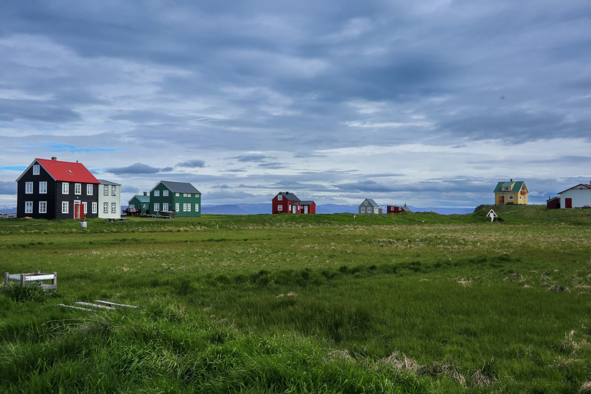 Colorful houses on a grassy field with a cloudy sky overhead.