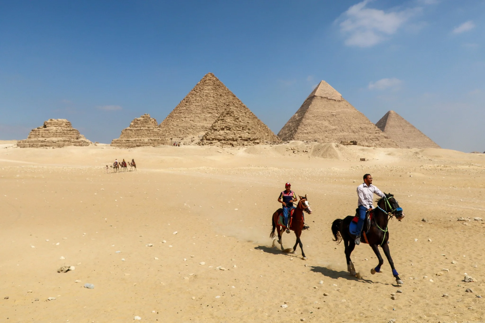 Tourists riding horses in the desert near the pyramids of Giza under a clear blue sky.