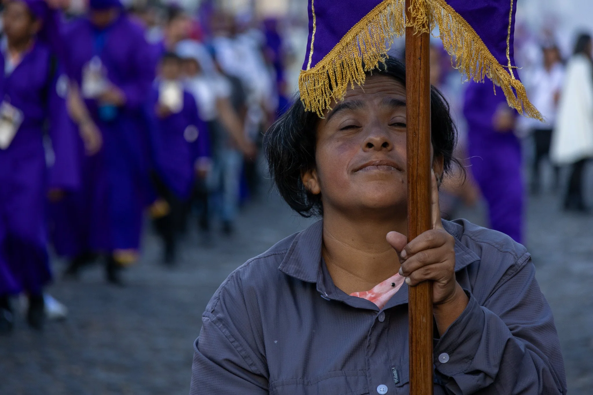 A woman holding a purple and gold parasol at a parade, with people in purple clothing in the background.