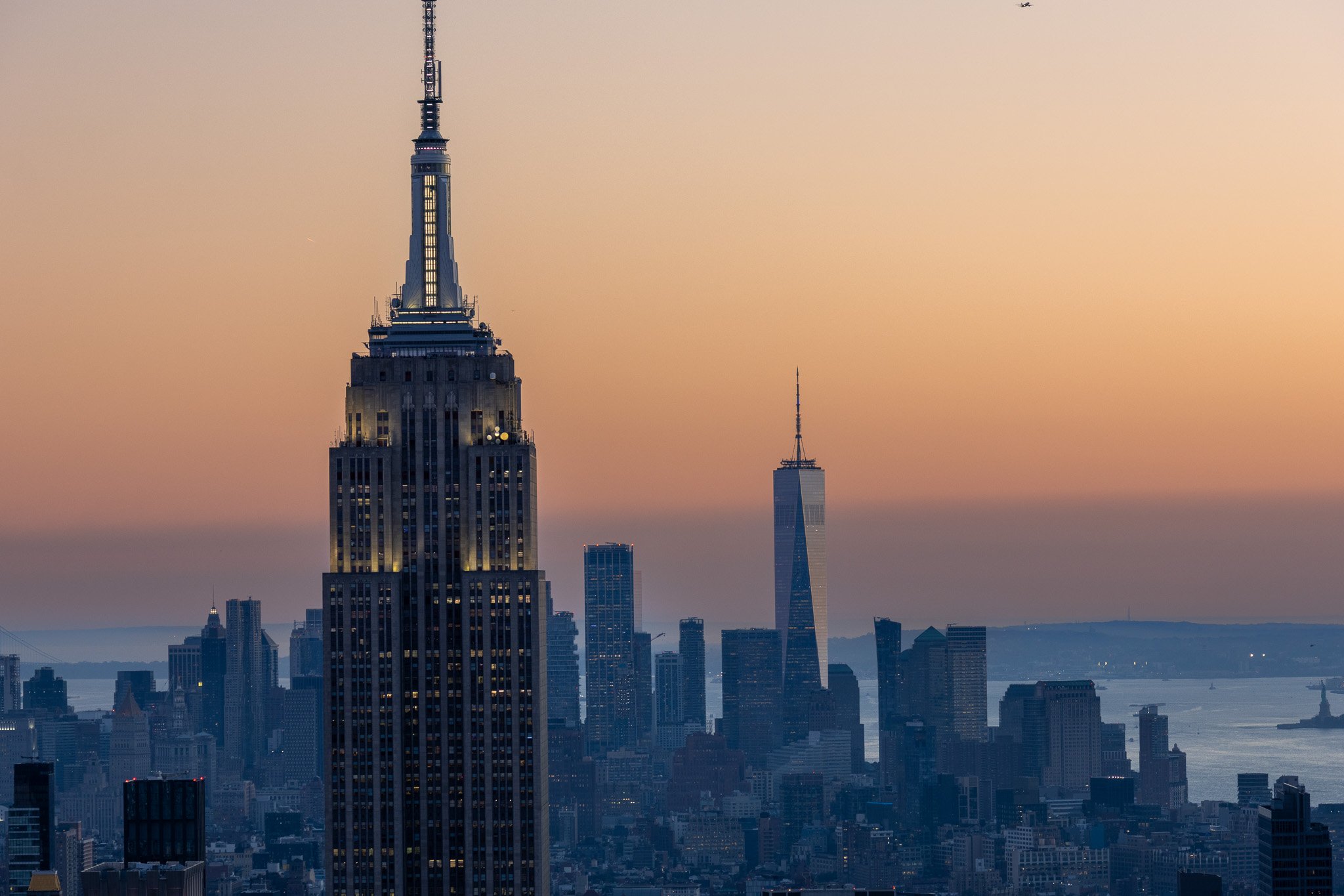 A city skyline at dusk featuring the Empire State Building and One World Trade Center in New York City.