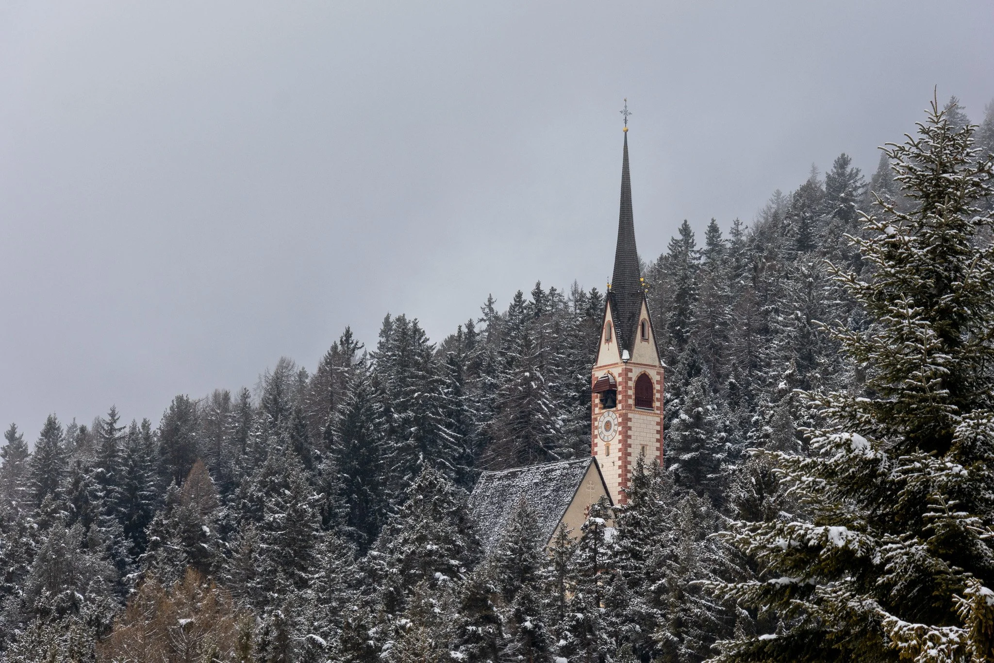 A church with a tall, pointed steeple surrounded by snow-covered trees in a mountainous area.
