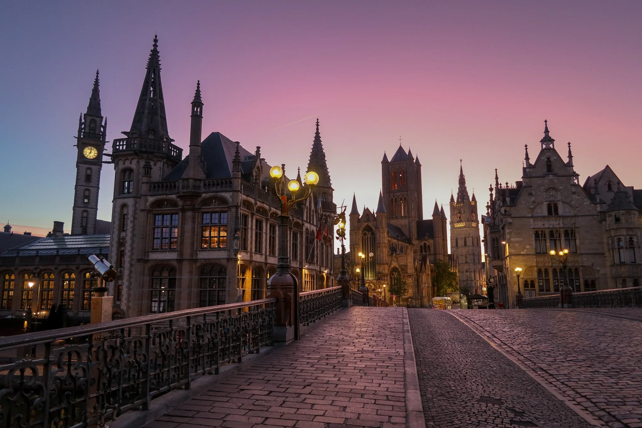 Historic European castle or cathedral during twilight with street lamps illuminating a cobblestone street.