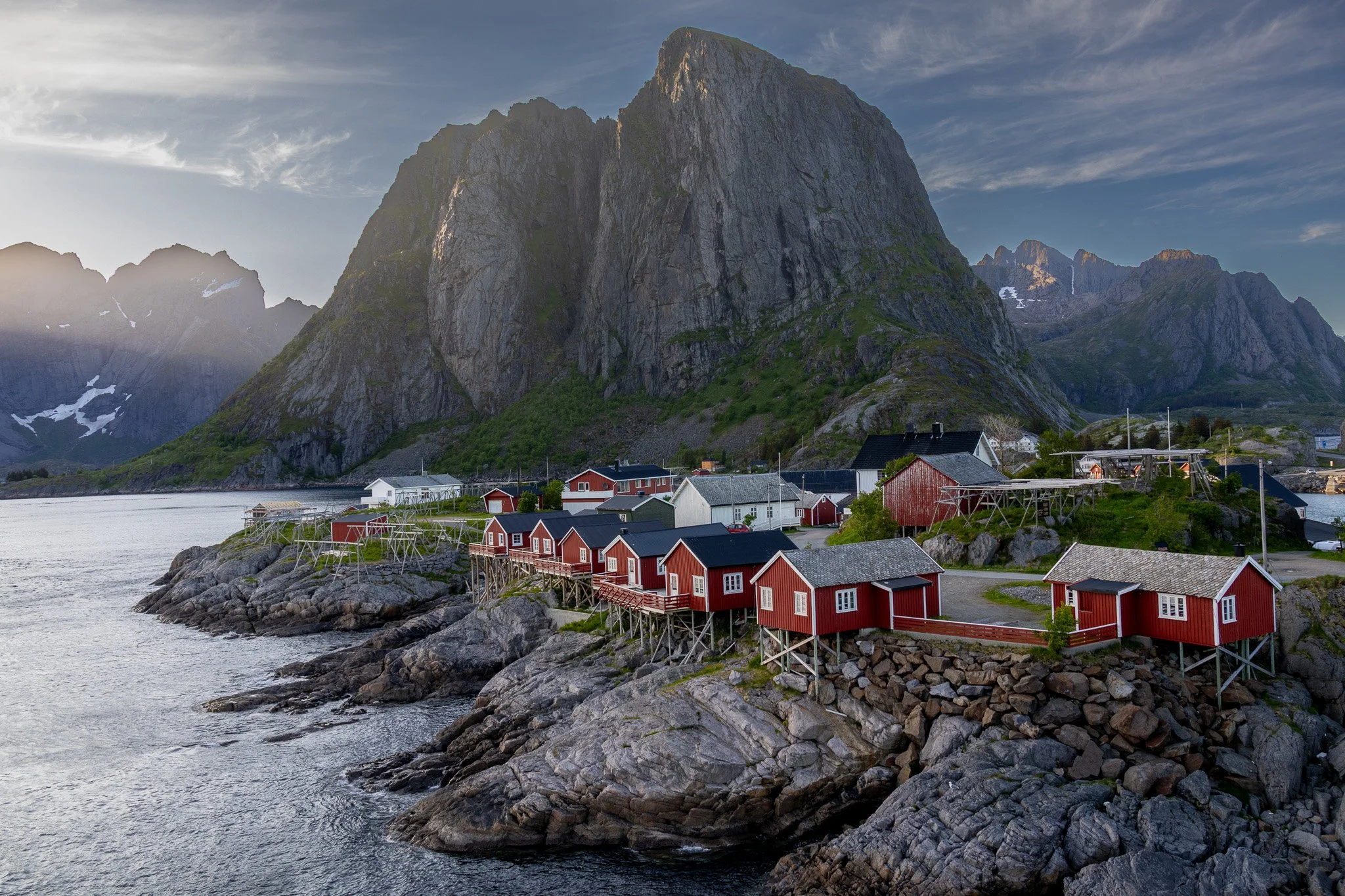 Colorful houses on stilts along a rocky shoreline with a large mountain in the background.
