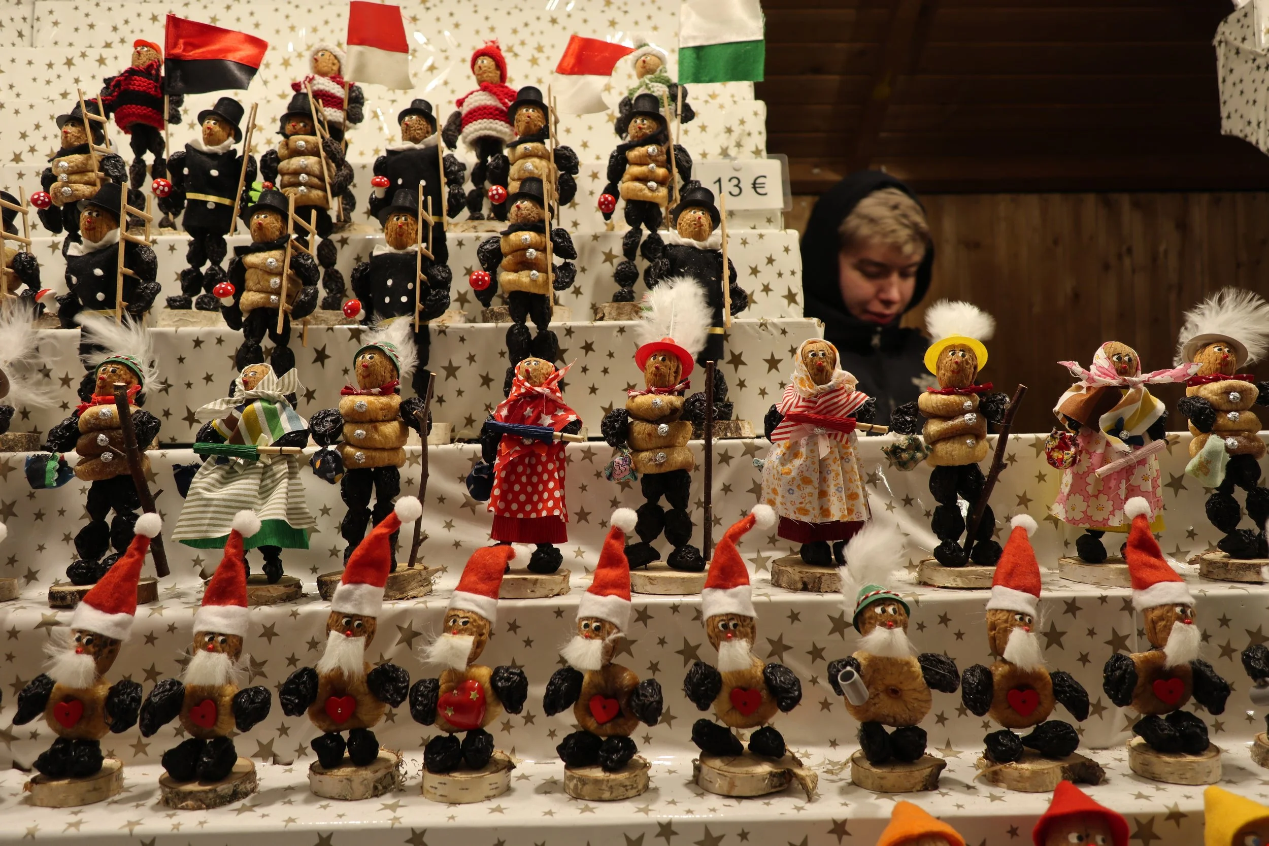 Display of handmade Christmas figurines resembling crows with Santa hats and accessories, arranged on tiered shelves.
