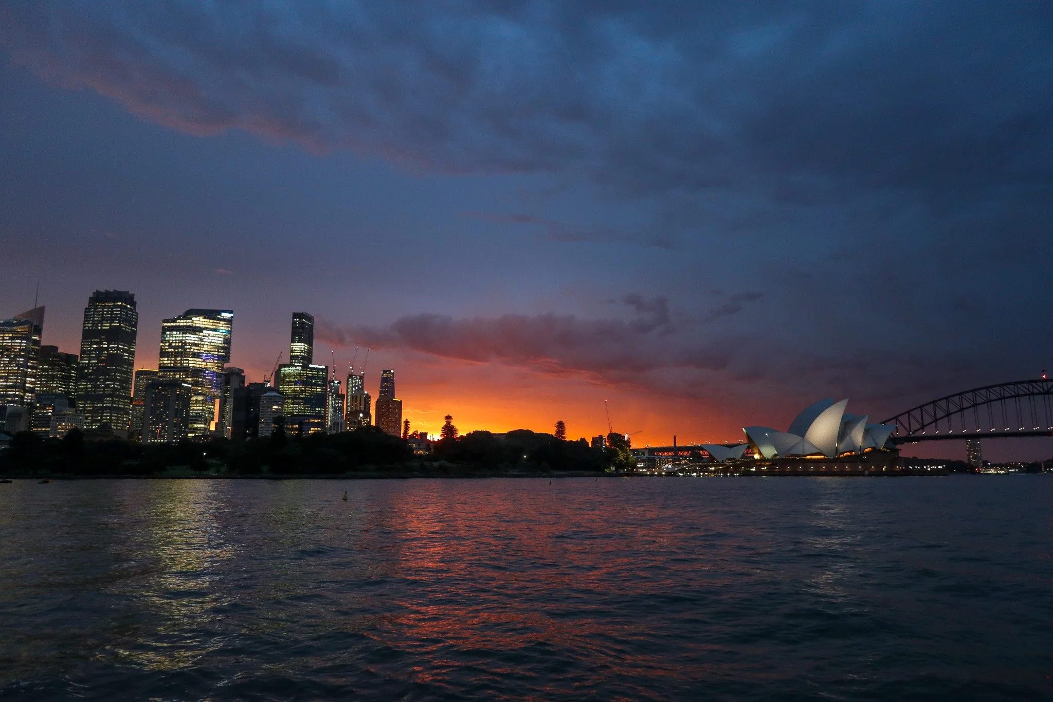 Sydney Opera House and city skyline at sunset viewed from across the water with clouds overhead.