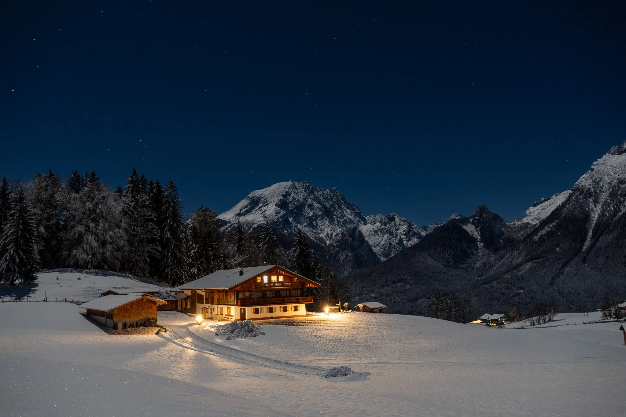 Snow-covered house at night with mountain range and starry sky in the background.