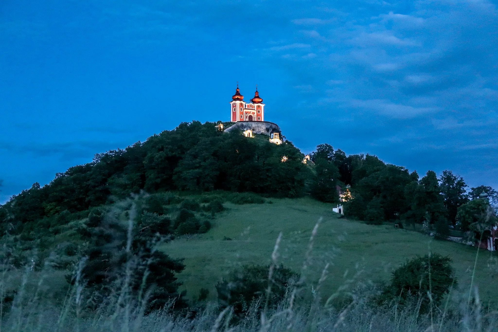 A church with two towers on a hilltop surrounded by trees during dusk.