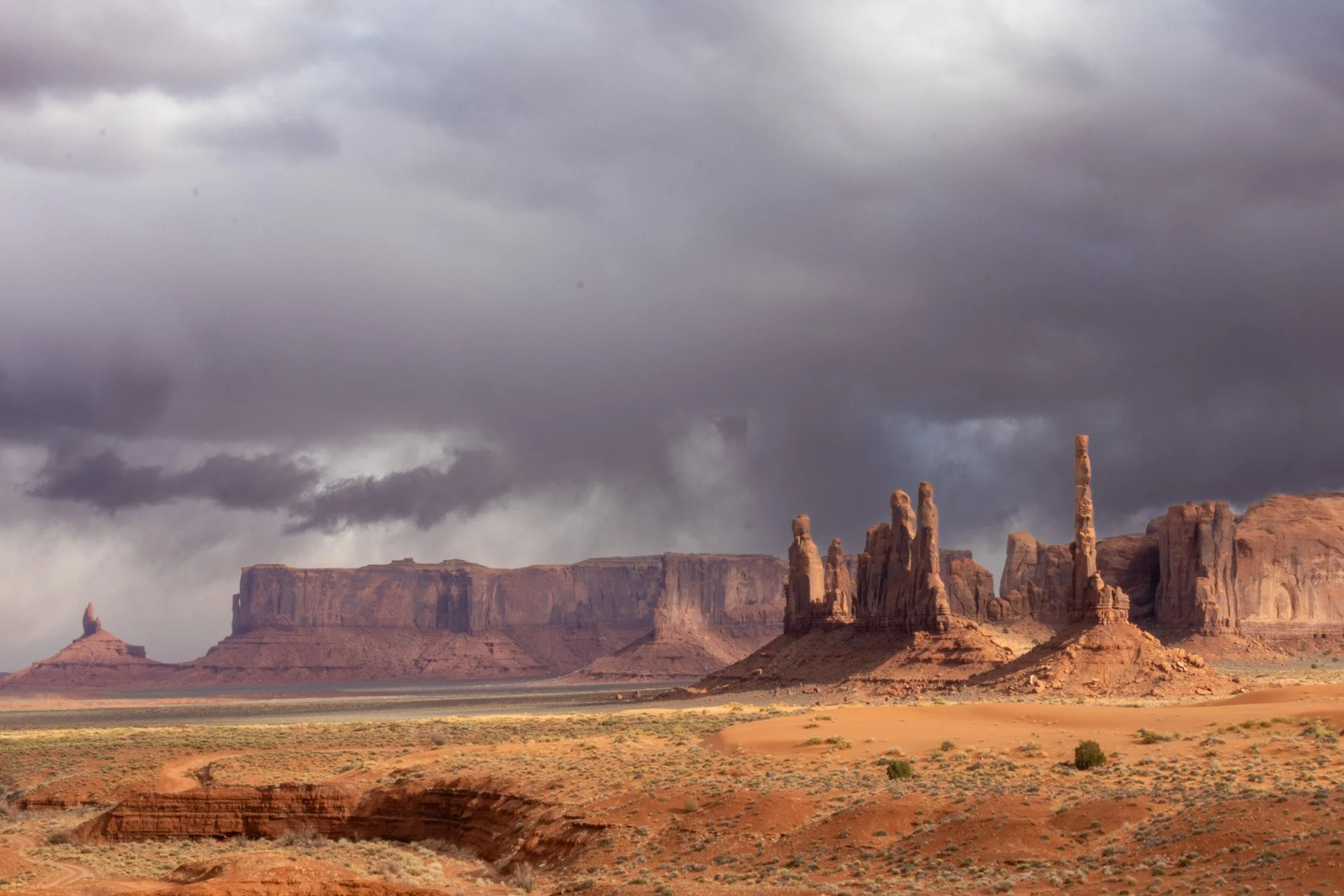 Desert landscape with large rock formations and mesas under a cloudy sky in Monument Valley.