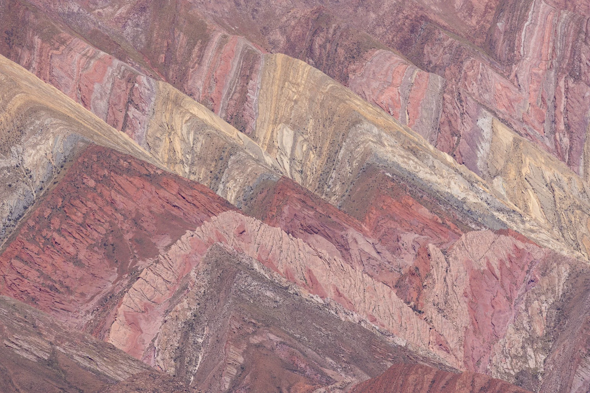 Colorful, diagonal rock formations with various shades of pink, purple, yellow, and brown in a mountainous landscape.