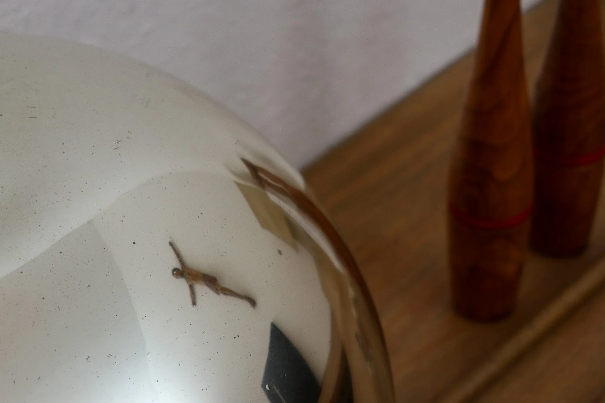 A small model figure of a person hanging on the interior of a round mirror.
