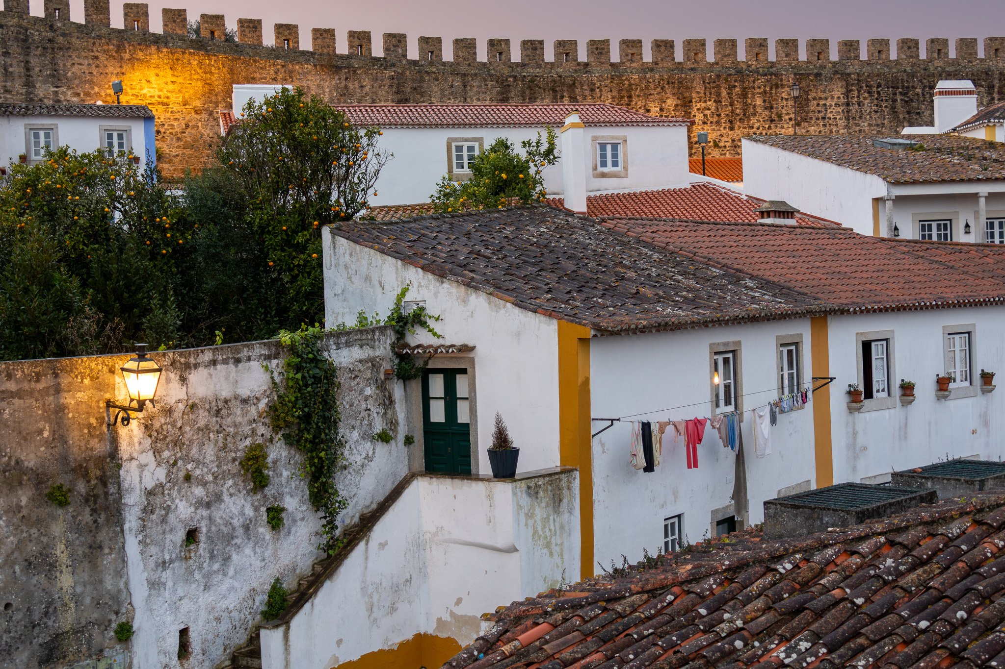 Historic white buildings with tiled roofs and laundry hanging outside, overlooking an ancient city wall at dusk.