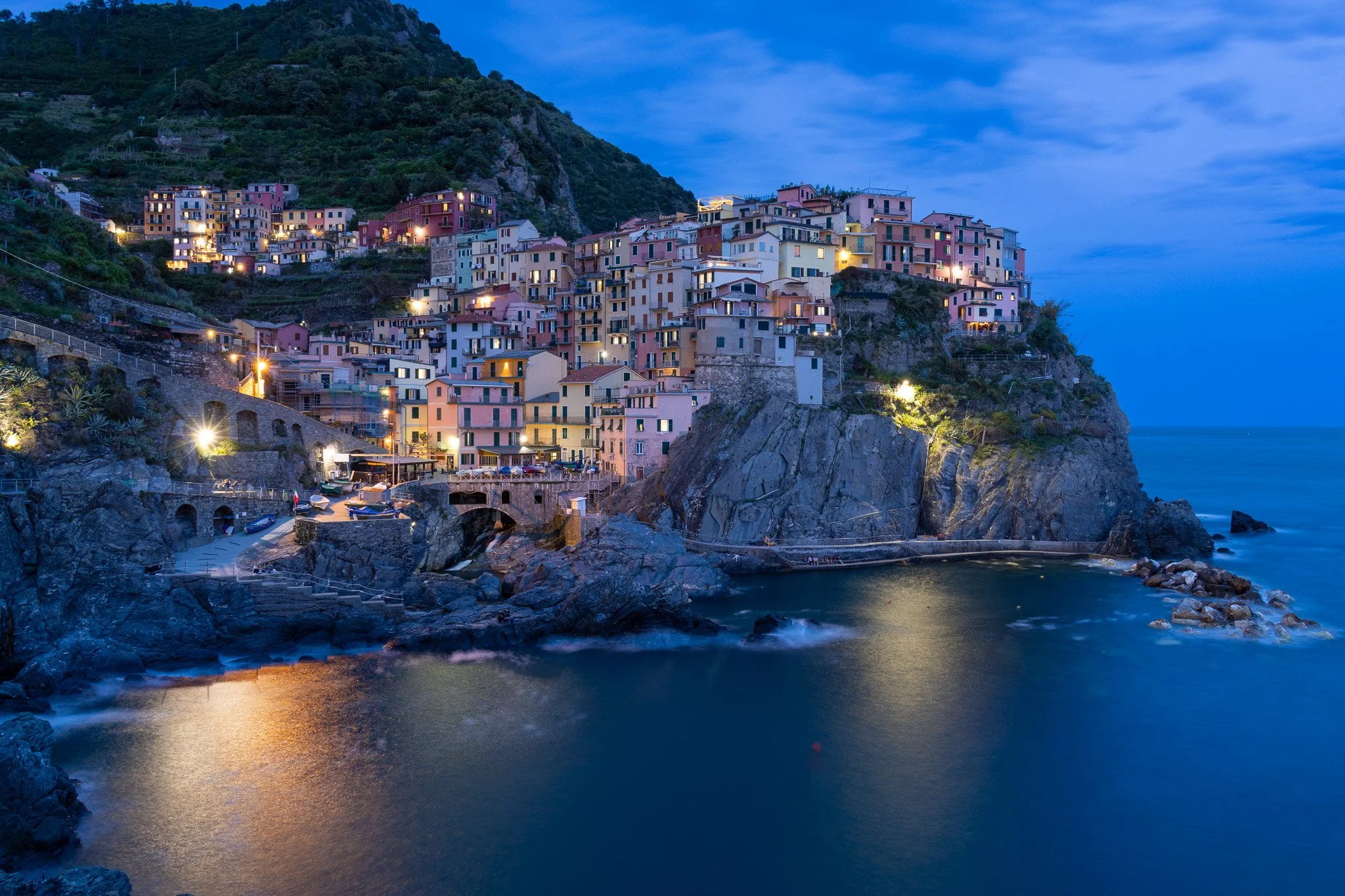 Colorful houses on a hillside overlooking the ocean at dusk, with lights glowing from the windows.