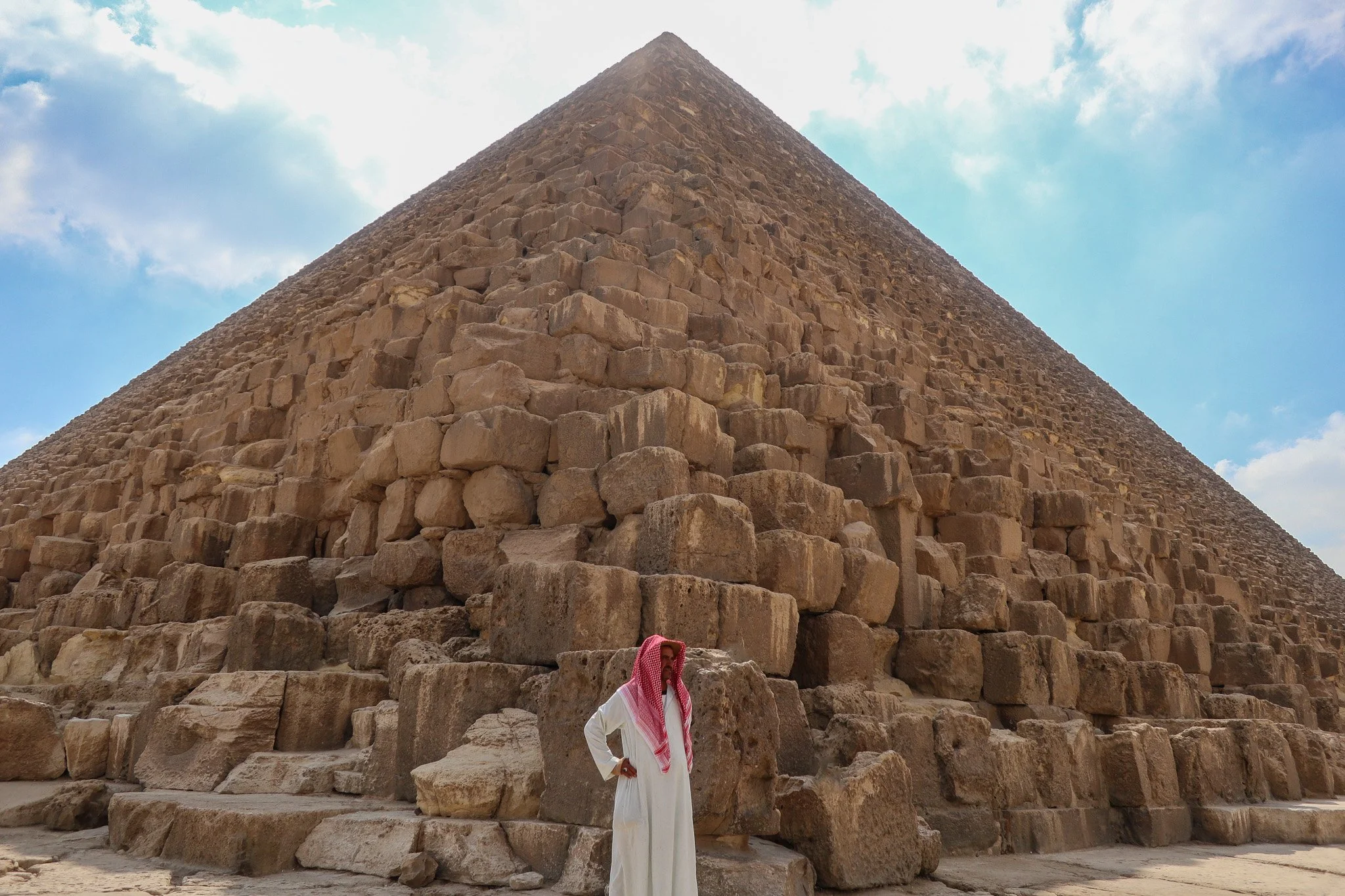 A person dressed in traditional Middle Eastern attire standing at the base of the Great Pyramid of Giza in Egypt.