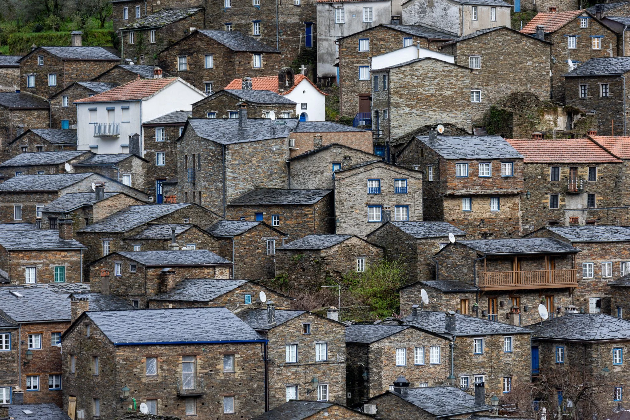 A hillside of closely packed stone houses with slate roofs, some with white or colored window frames, satellite dishes, and small balconies.