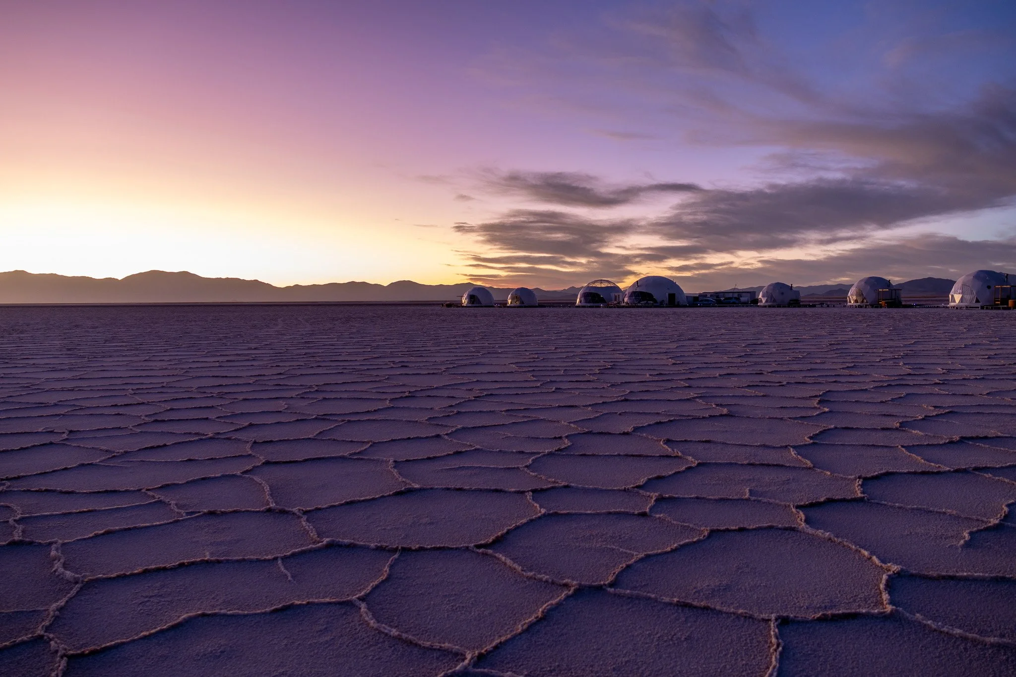 Salt flats at sunrise with geodesic domes in the distance and mountains on the horizon.