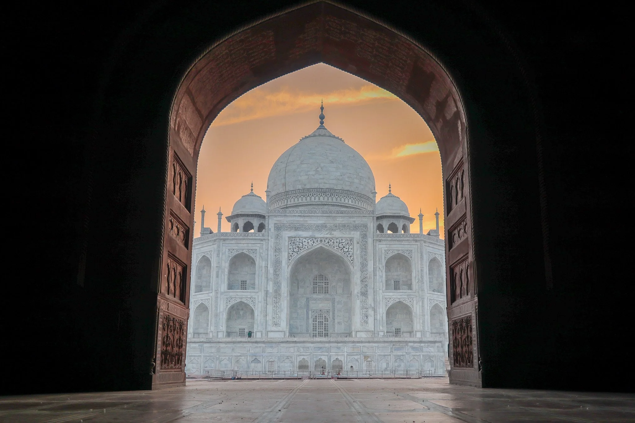 View of the Taj Mahal through an ornate archway at sunrise or sunset.
