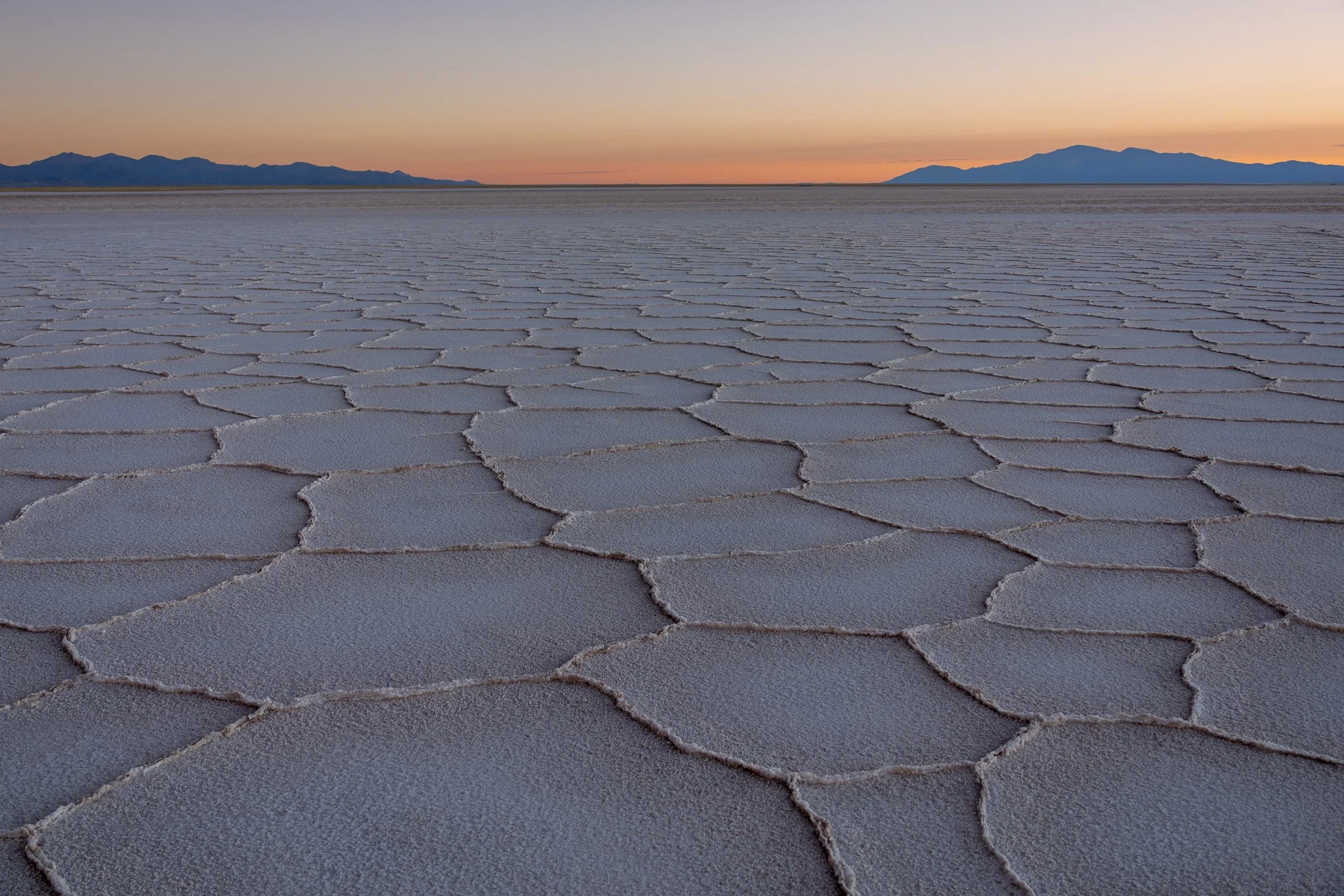Salt flats at sunset with cracked salt surface and distant mountains.