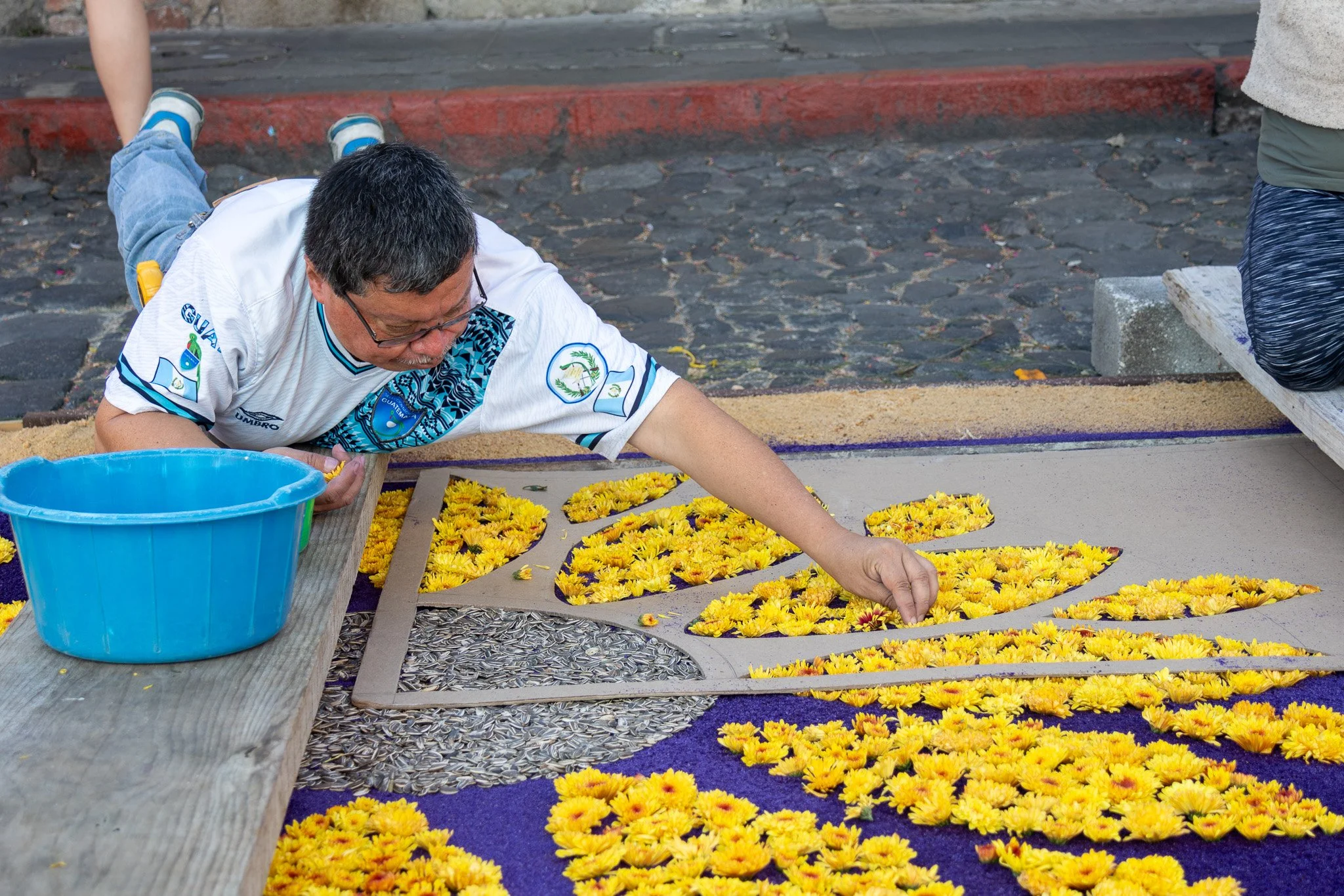 Man arranging yellow flowers on a decorative design for a cultural or religious event.