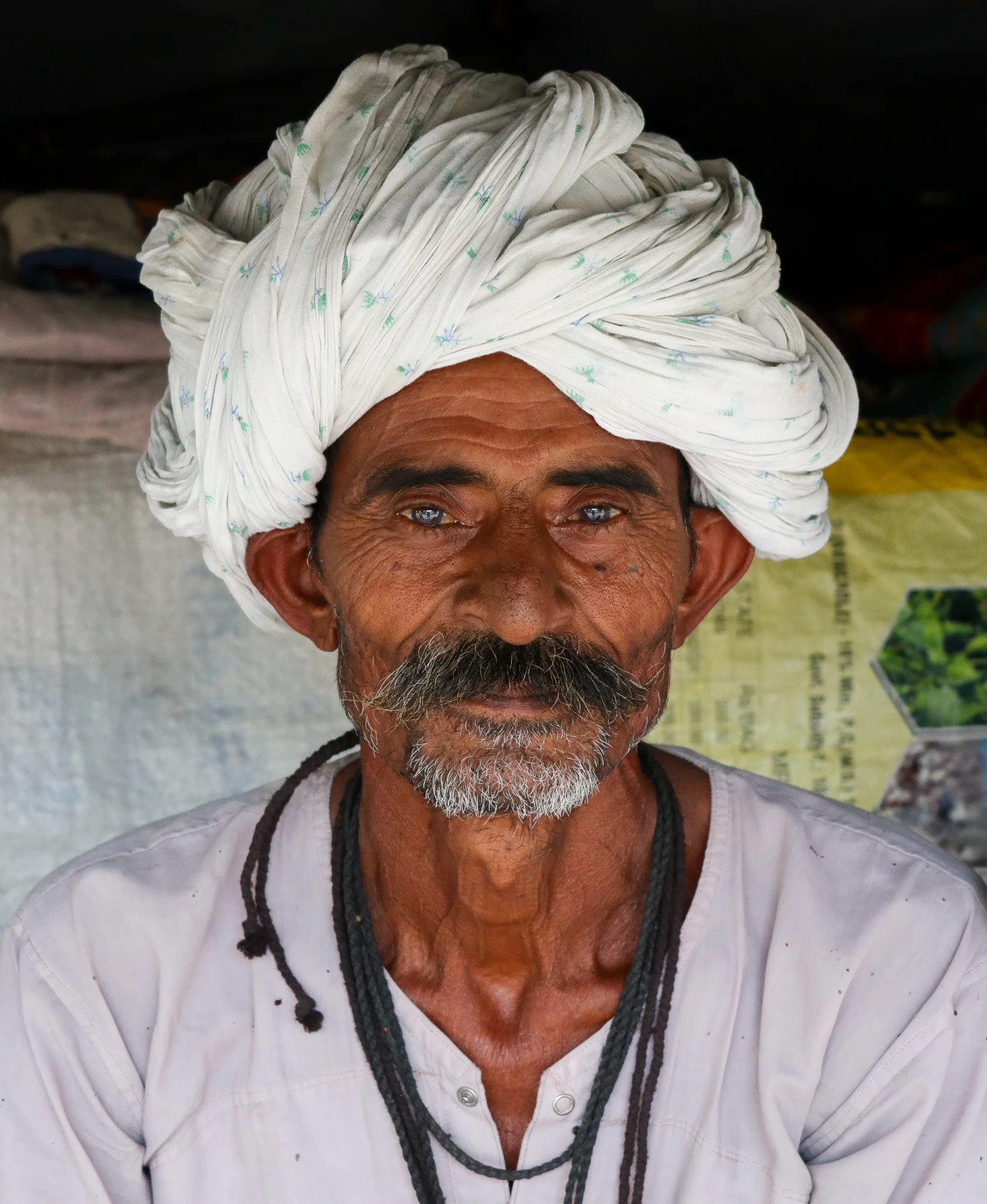A portrait of an elderly man with a weathered face, gray beard, and wearing a white turban and white shirt.
