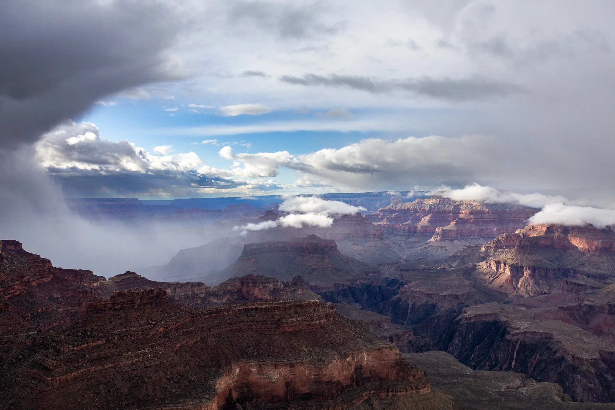 A view of the Grand Canyon with layered rock formations, clouds, and a partly cloudy sky.