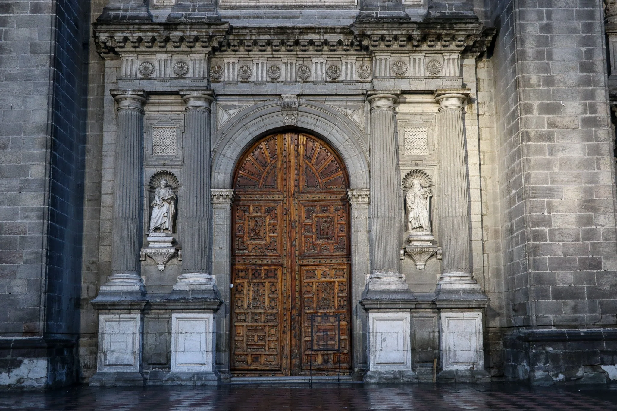 A large, ornate wooden door framed by stone columns and statues on the exterior of a historic building, possibly a cathedral or church.