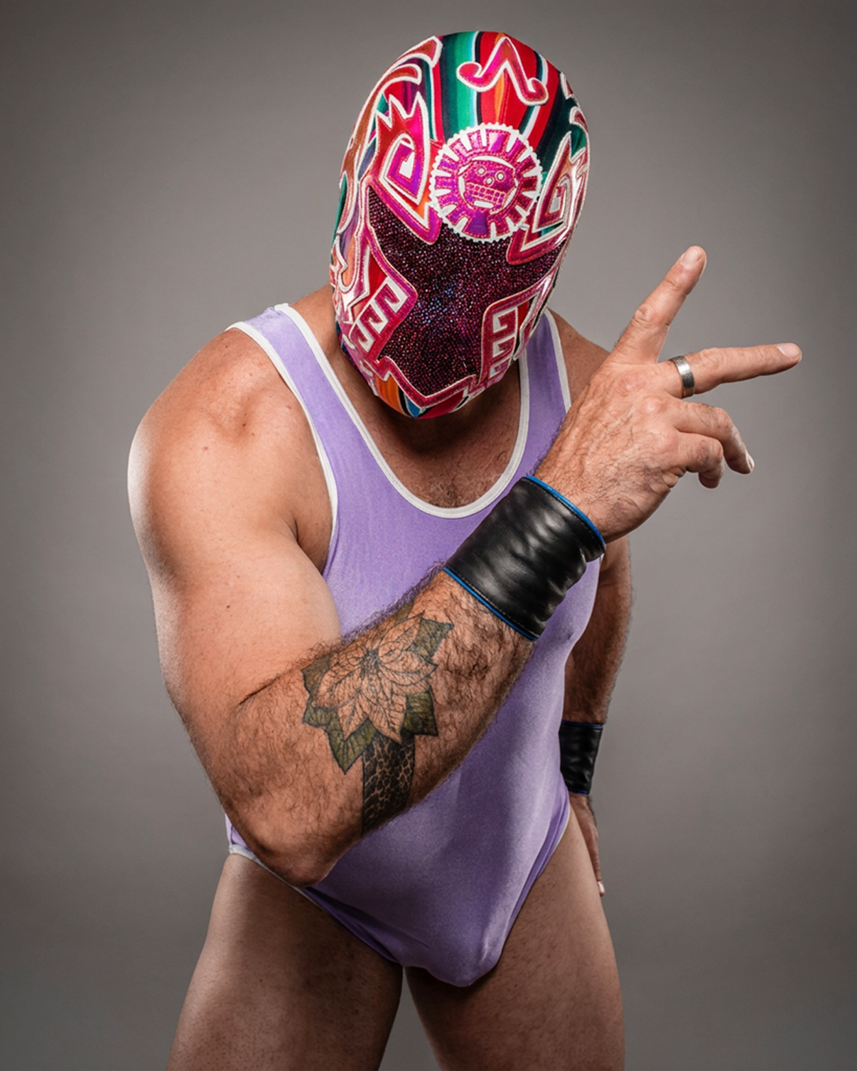 The masked luchador Nagual poses in a colorful mask and lavender spandex leotard, gray background