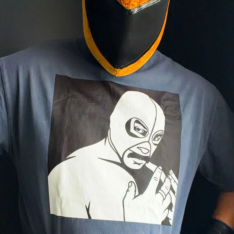 Closeuo of the masked luchador Nagual wearing a t-shirt with his own masked face on the graphic