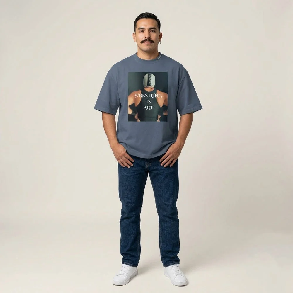 Front view of the Wrestling Is Art oversized tee in faded indigo, worn full-length with jeans