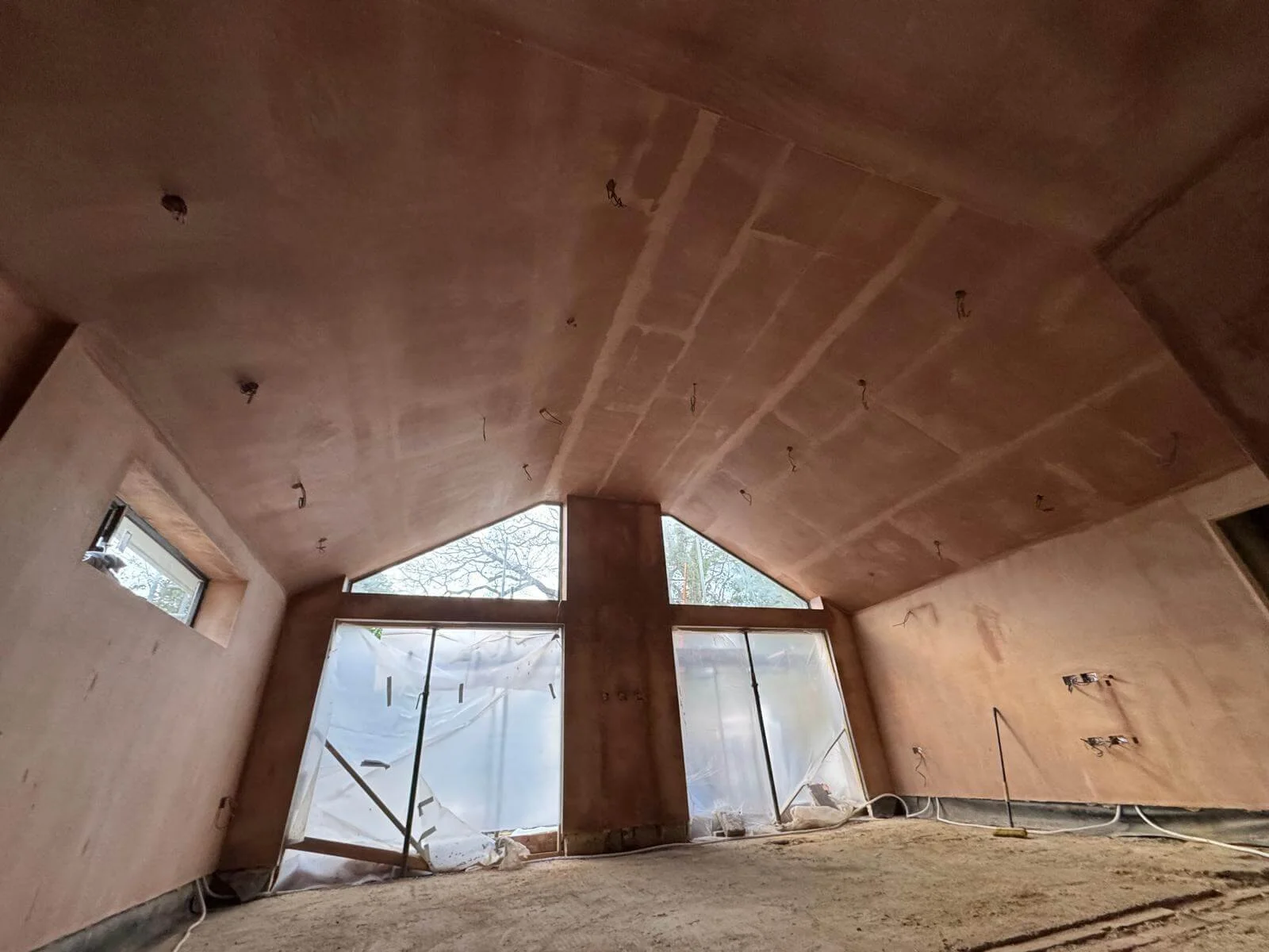 Interior of a room under construction with a wooden ceiling, large front windows, and unfinished walls and floors.