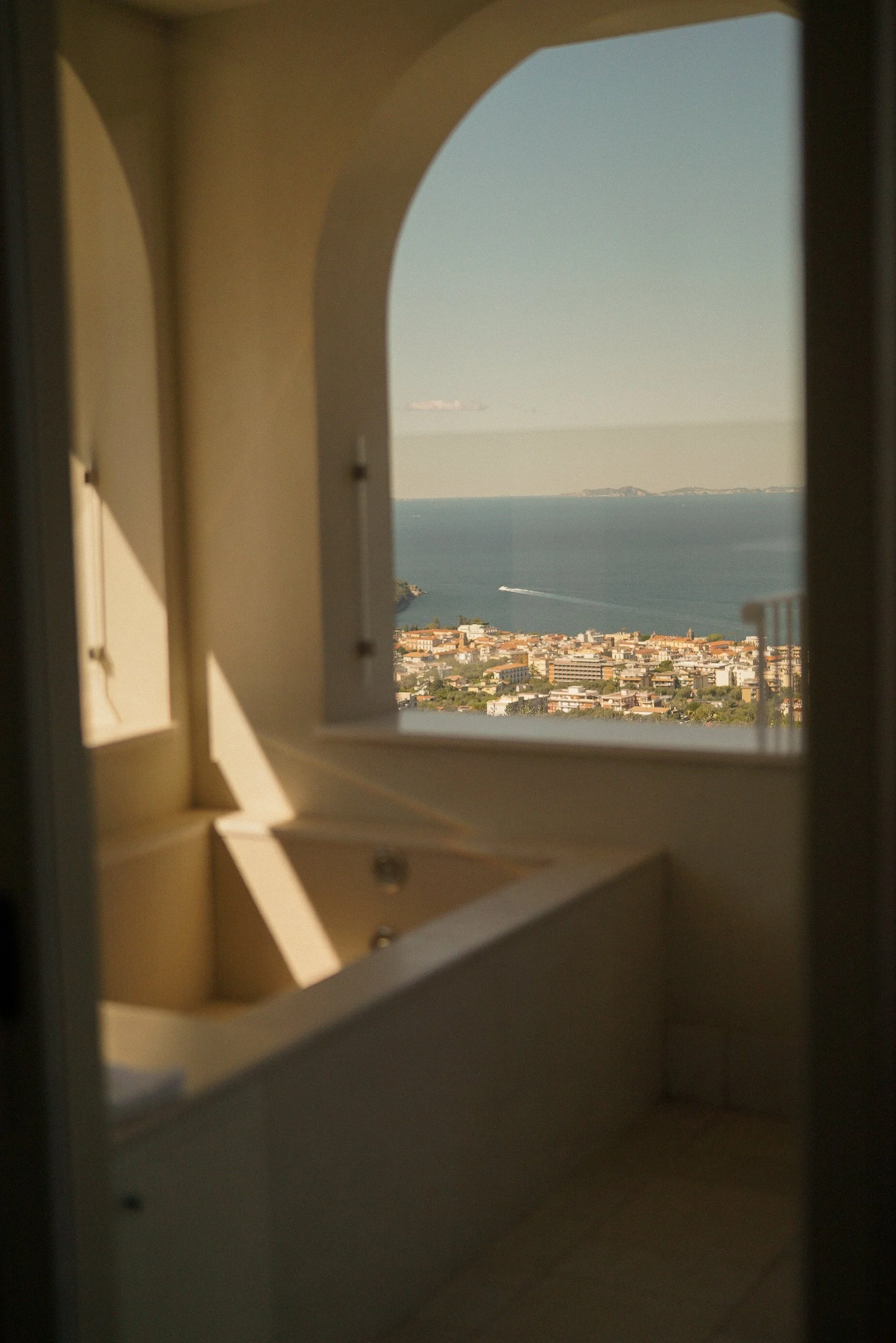 View through a window showing a cityscape, water, and distant hills.