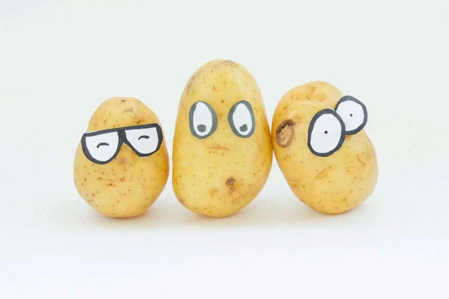 Three potatoes with cartoon face drawings, each with different expressions, on a white background.