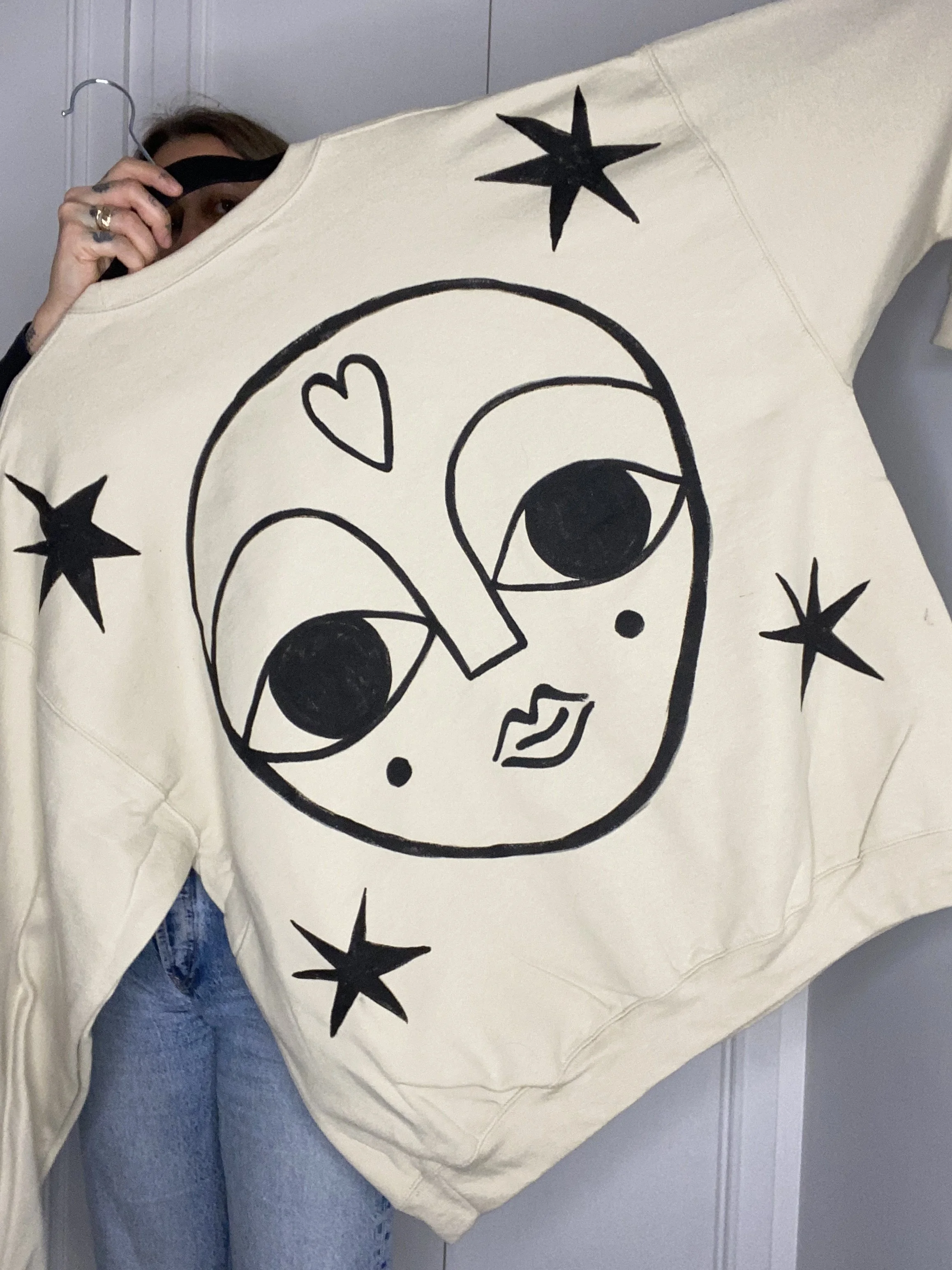 Person holding a large blanket with a black outline drawing of a cartoon face with big eyes, lips, a heart, and stars around it.