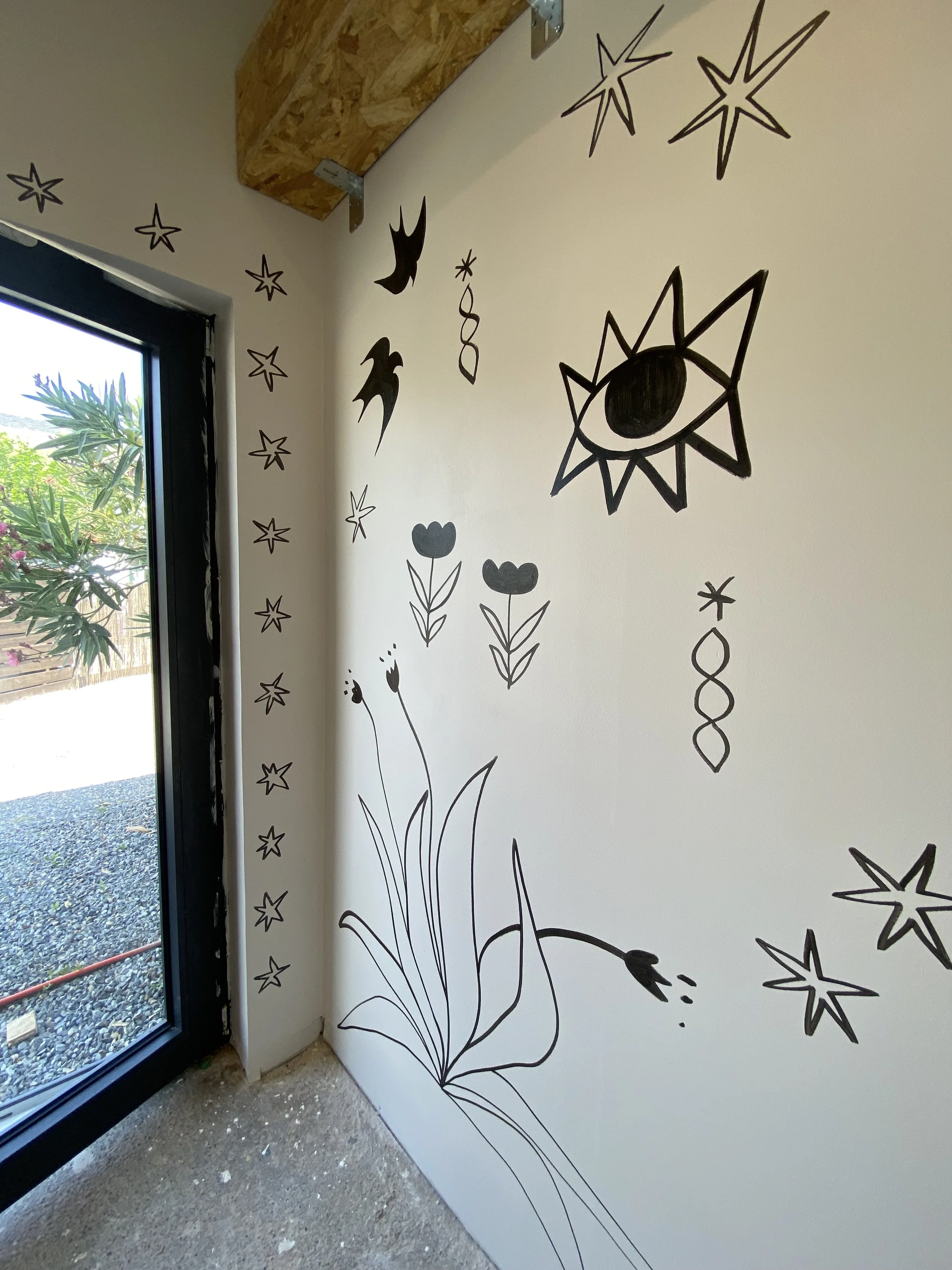 Decorative black sticker artwork on a wall featuring stars, eyes, flowers, and abstract shapes.