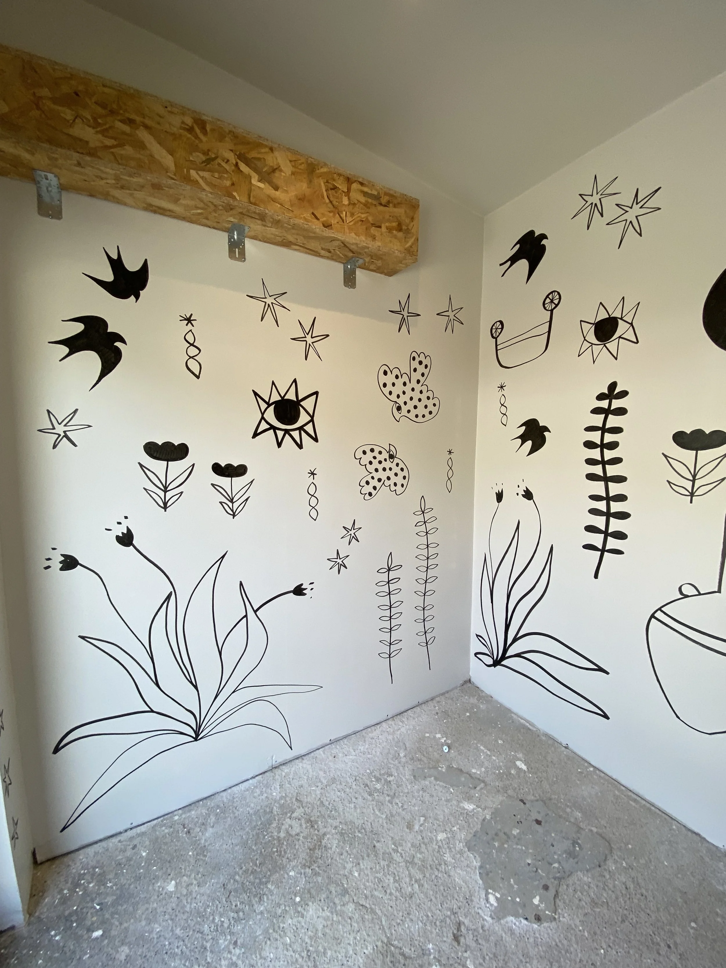 Black line drawings of flowers, leaves, stars, birds, and butterflies on white walls, with a wooden support beam attached near the ceiling.